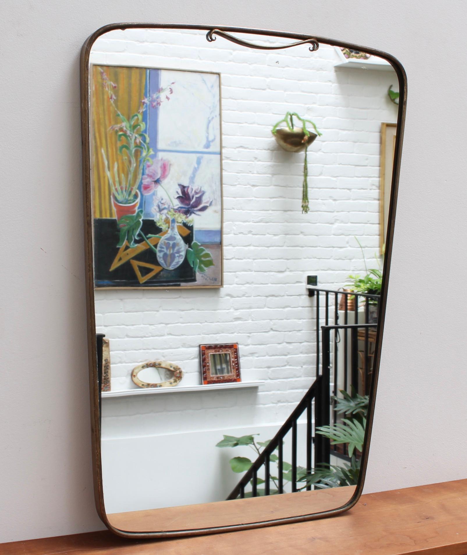 Midcentury Italian wall mirror with brass frame and flourish (circa 1950s). The mirror is rather large, unusually but beautifully-shaped, somewhat like a slice of white bread. It is classically elegant in a modern Gio Ponti style. The mirror is in