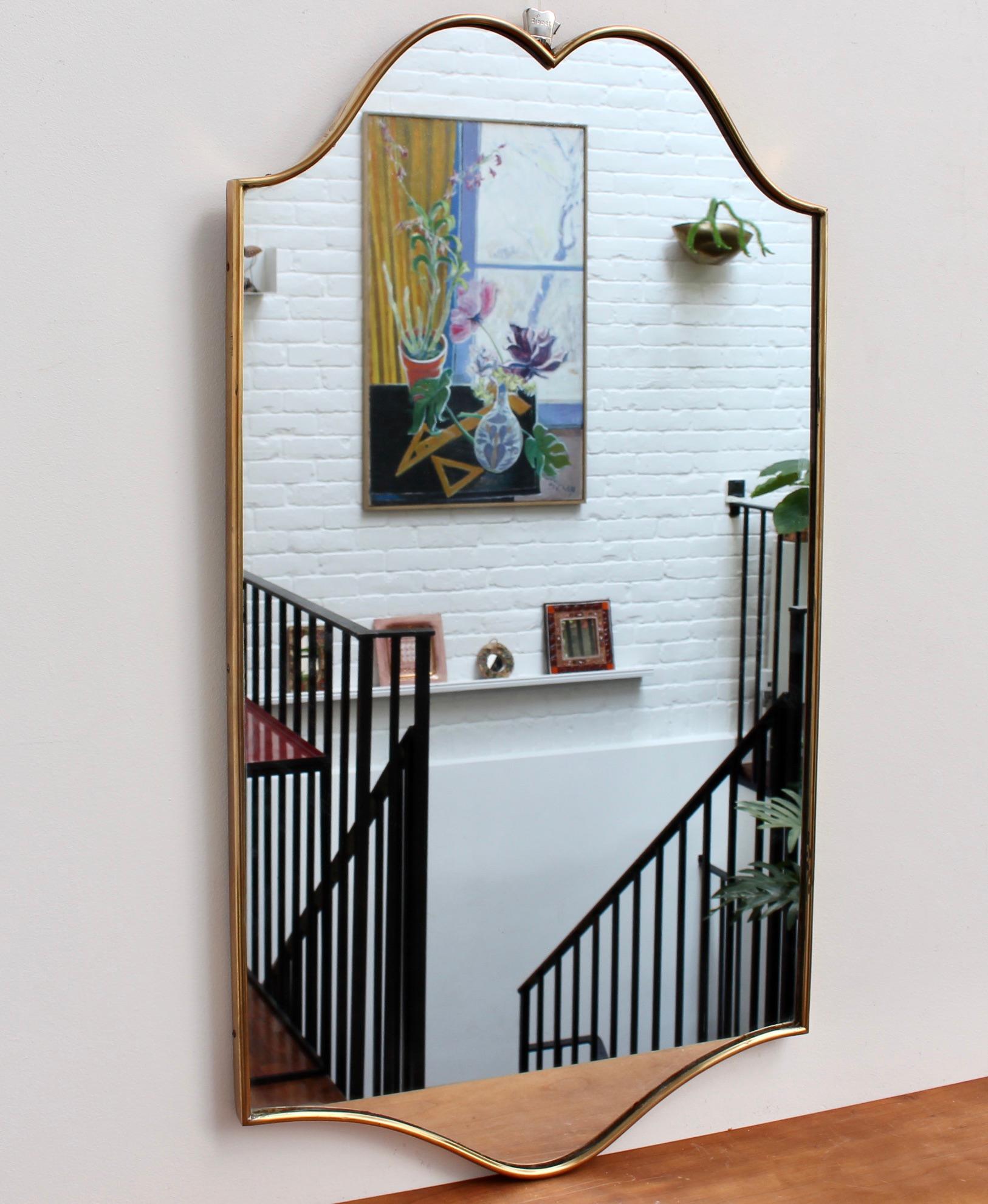 Midccentury Italian wall mirror with brass frame (circa 1950s). The mirror sports ruggedly straight lines accented on both top and bottom by sensuous curves -classically elegant and distinctive in a modern Gio Ponti style. This mirror is in good