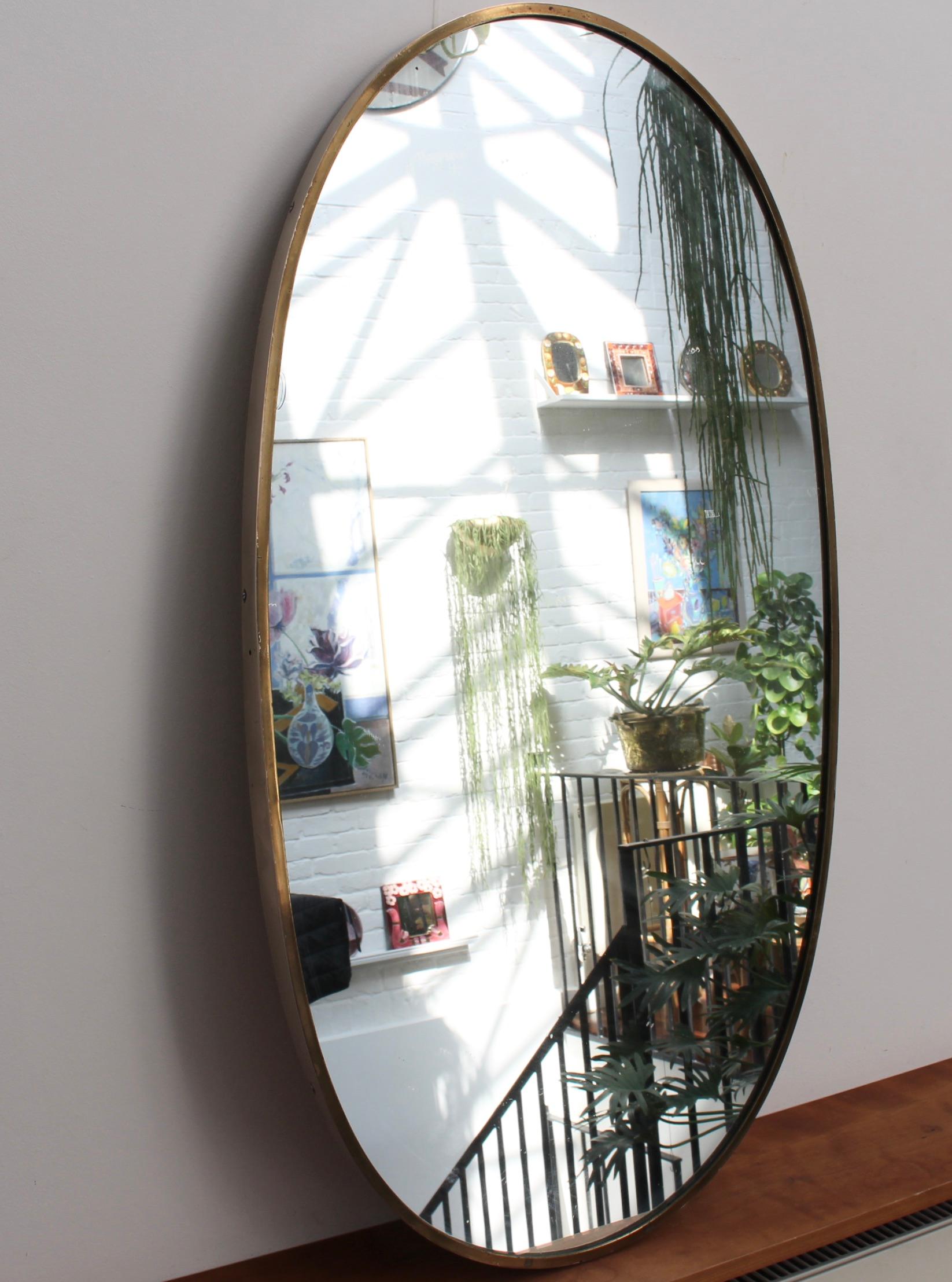 Mid-century Italian wall mirror with brass frame, (circa 1950s). A very sizeable and weighty oval mirror which has retained its smartness coupled with an irresistible charm. The visual impression is elegant and very distinctive in a modern Gio Ponti