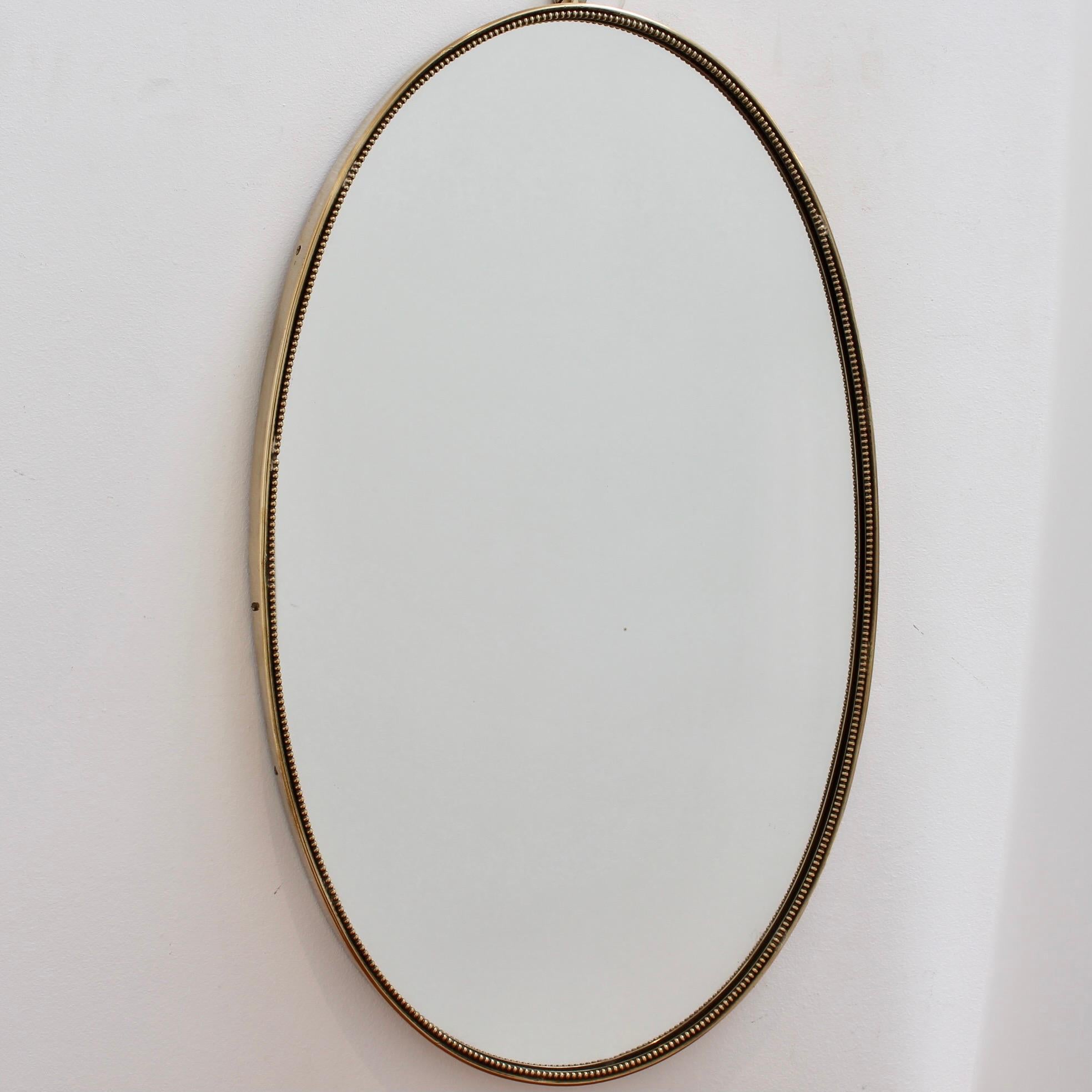 Mid-century Italian wall mirror with brass frame (circa 1950s). The mirror is oval in shape, very smart with irresistible durability. The visual impression is elegant and very distinctive in a modern Gio Ponti style. A distinctive beading outlines