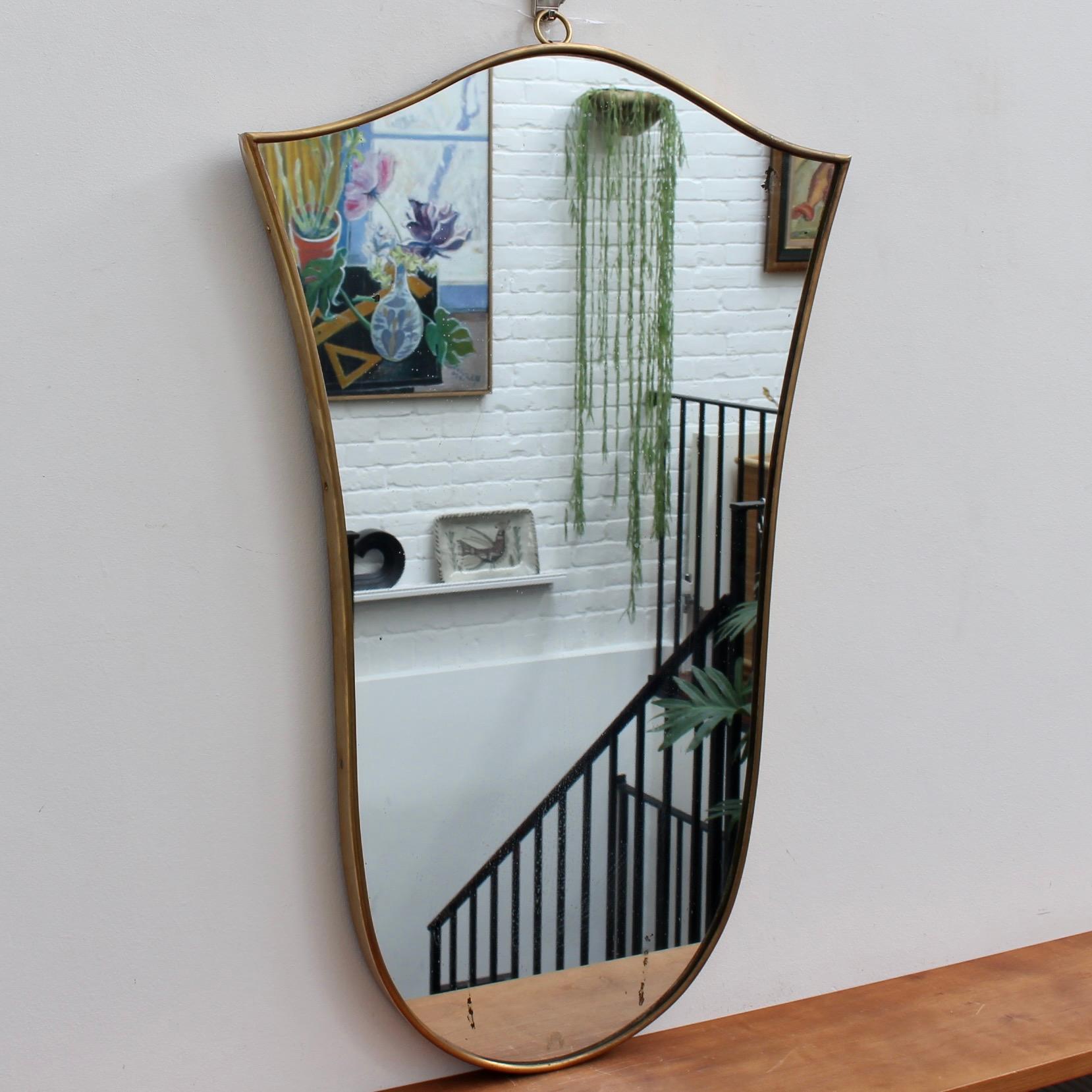 Mid-Century Italian wall mirror with brass frame (circa 1950s). This mirror has sensuous curves yet retains its solidity and imposing good looks. The tulip-shape is rarely found in this style of mirror. It is in fair vintage condition with several