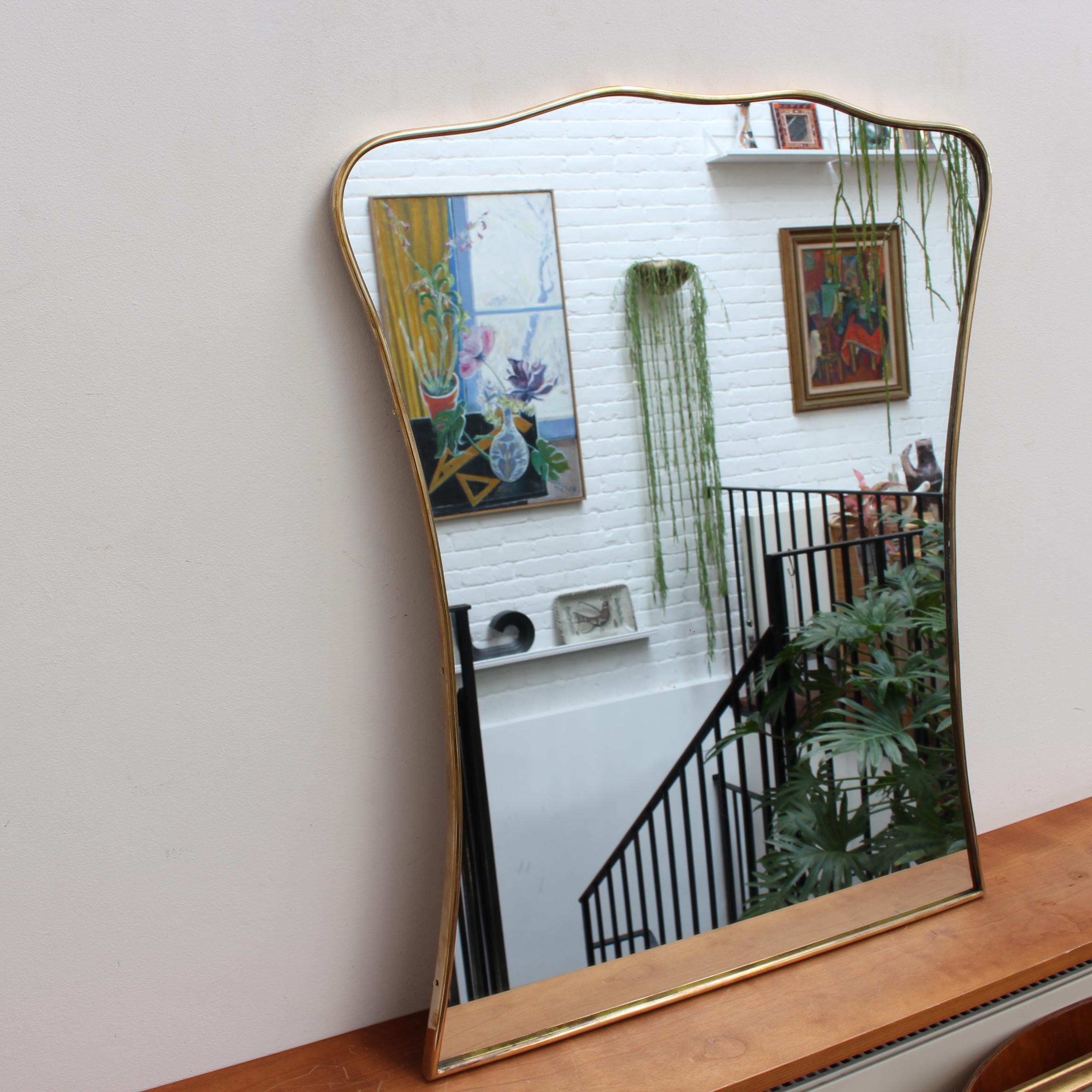 Mid-century Italian wall mirror with brass frame (circa 1950s). The smart, sturdy mirror sports a very original and delightful shape. Like other mirrors in this style, they are always classically elegant and distinctive. In good overall condition; a
