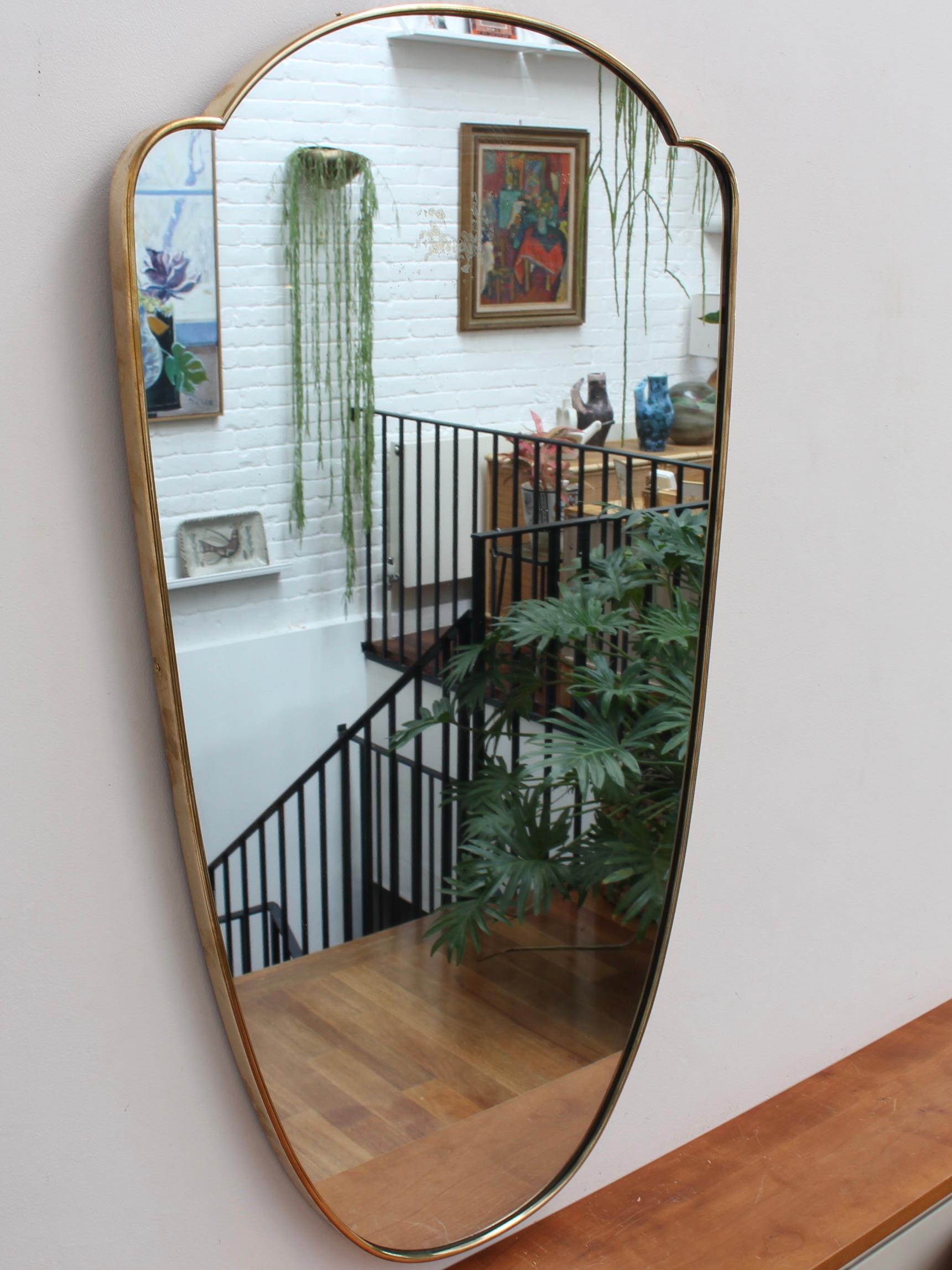 Mid-century Italian wall mirror with brass frame (circa 1950s). The mirror is classically-shaped and distinctive in a Gio Ponti style. The frame is in good overall condition with a characterful, age-related patina. The mirror is in fair condition