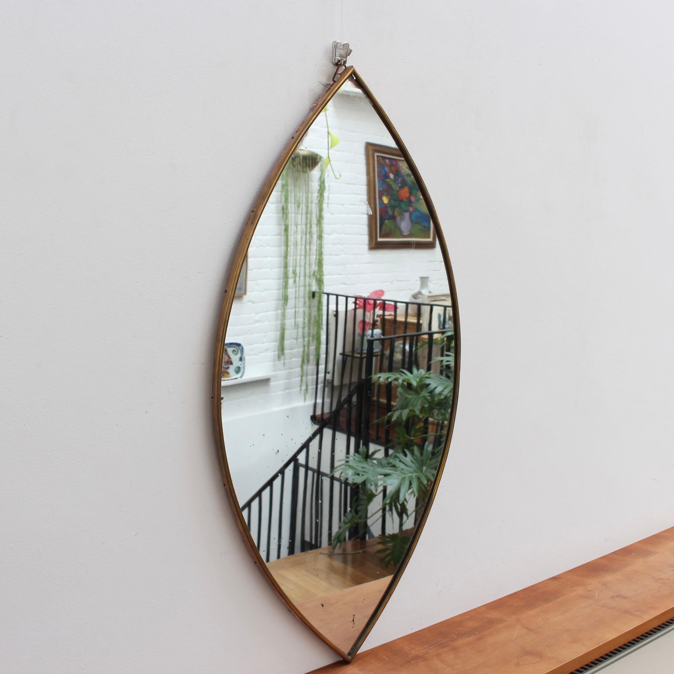 Mid-Century Italian wall mirror with brass frame (circa 1950s). This mirror is elegant and characterful in a modern style. It is a leaf-shaped piece in fair overall condition. A patina covers much of the brass frame. Please note there are some
