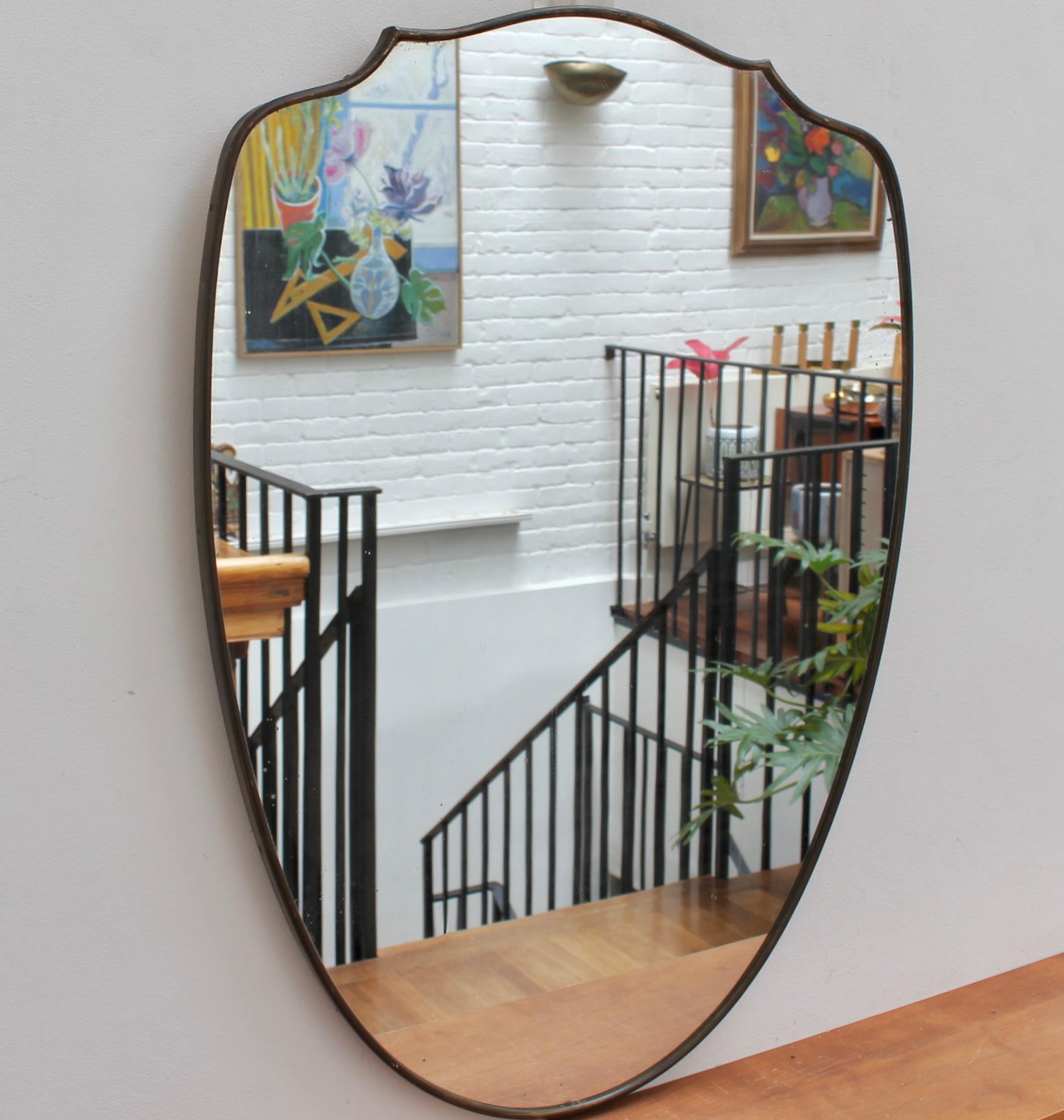 Mid-century Italian wall mirror with brass frame (circa 1950s). The mirror is classically-shaped and distinctive in a Modern style. It is in fair overall condition considering the presence of a small malformation in the glass near the base (see