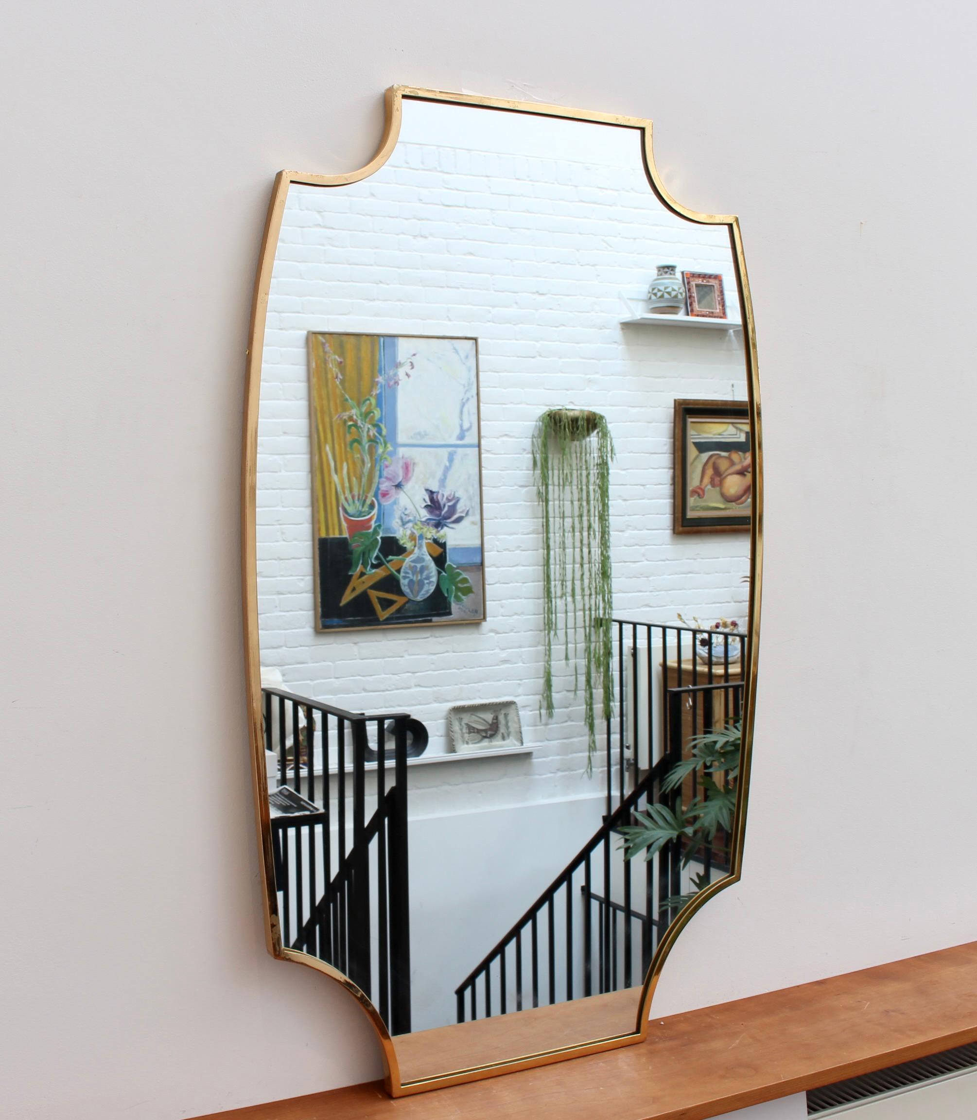 Mid-century Italian wall mirror with brass frame (circa 1950s). The sizeable and weighty mirror sports a very original and delightful shape which is like that single missing piece of a puzzle. Like other mirrors in this style, they are always