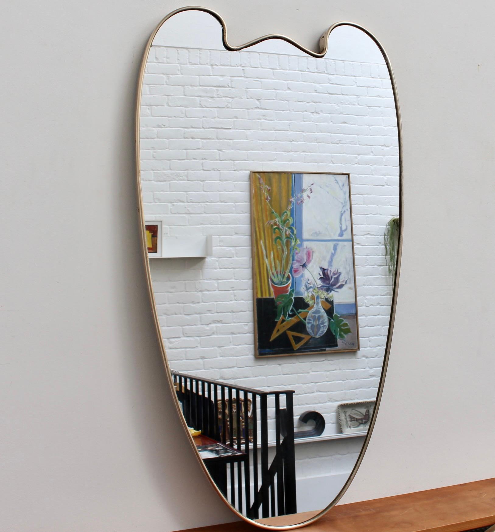 Large mid-century Italian wall mirror with brass frame (circa 1950s). The mirror is classically-shaped and distinctive in a Gio Ponti style. This mirror is in good overall condition. There are some characterful blemishes and a beautiful patina on