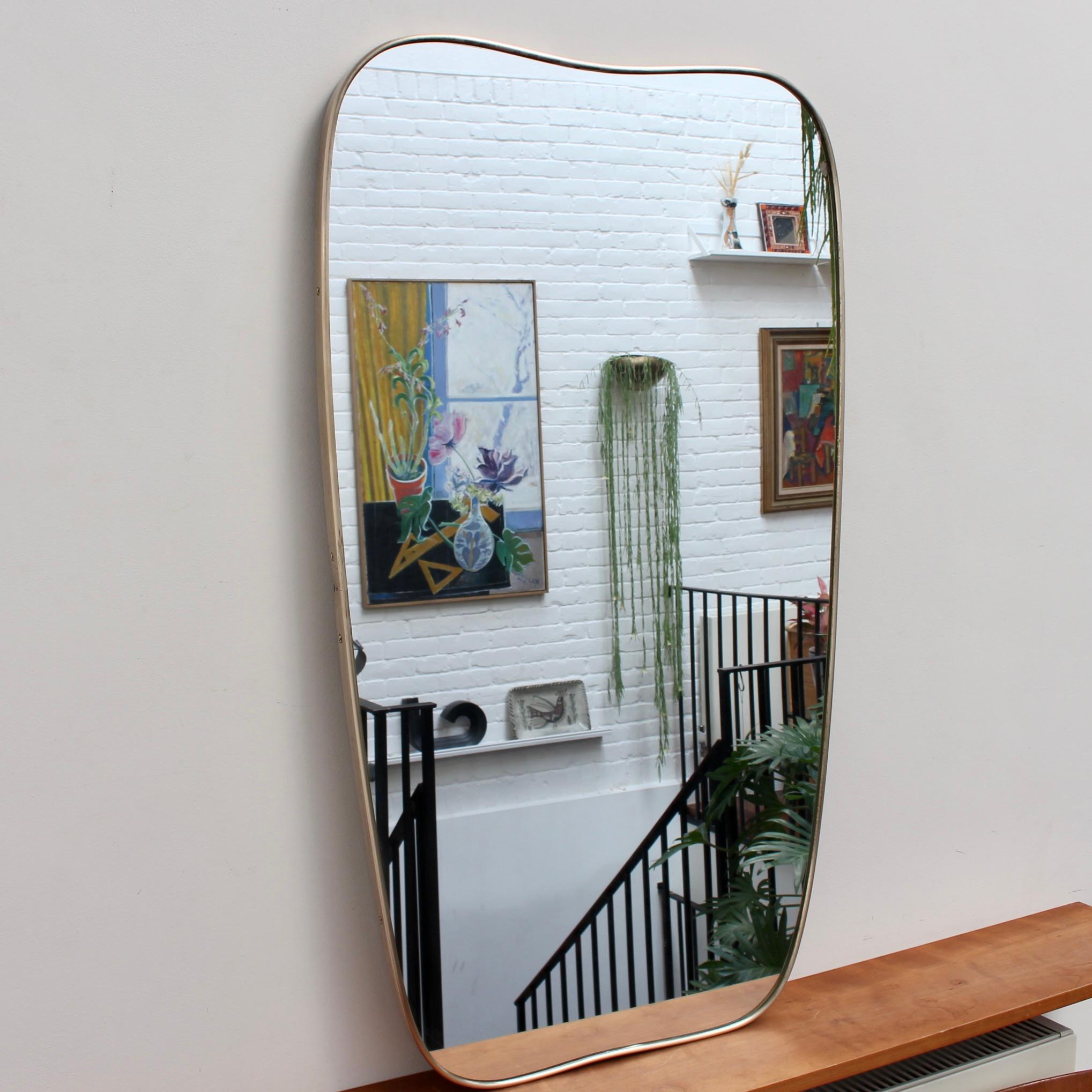 Large Mid-Century Italian wall mirror with brass frame (circa 1950s). The mirror is classically-shaped and distinctive in a Gio Ponti style. This mirror is in good overall condition notwithstanding the chip and blemish evident in the glass (please
