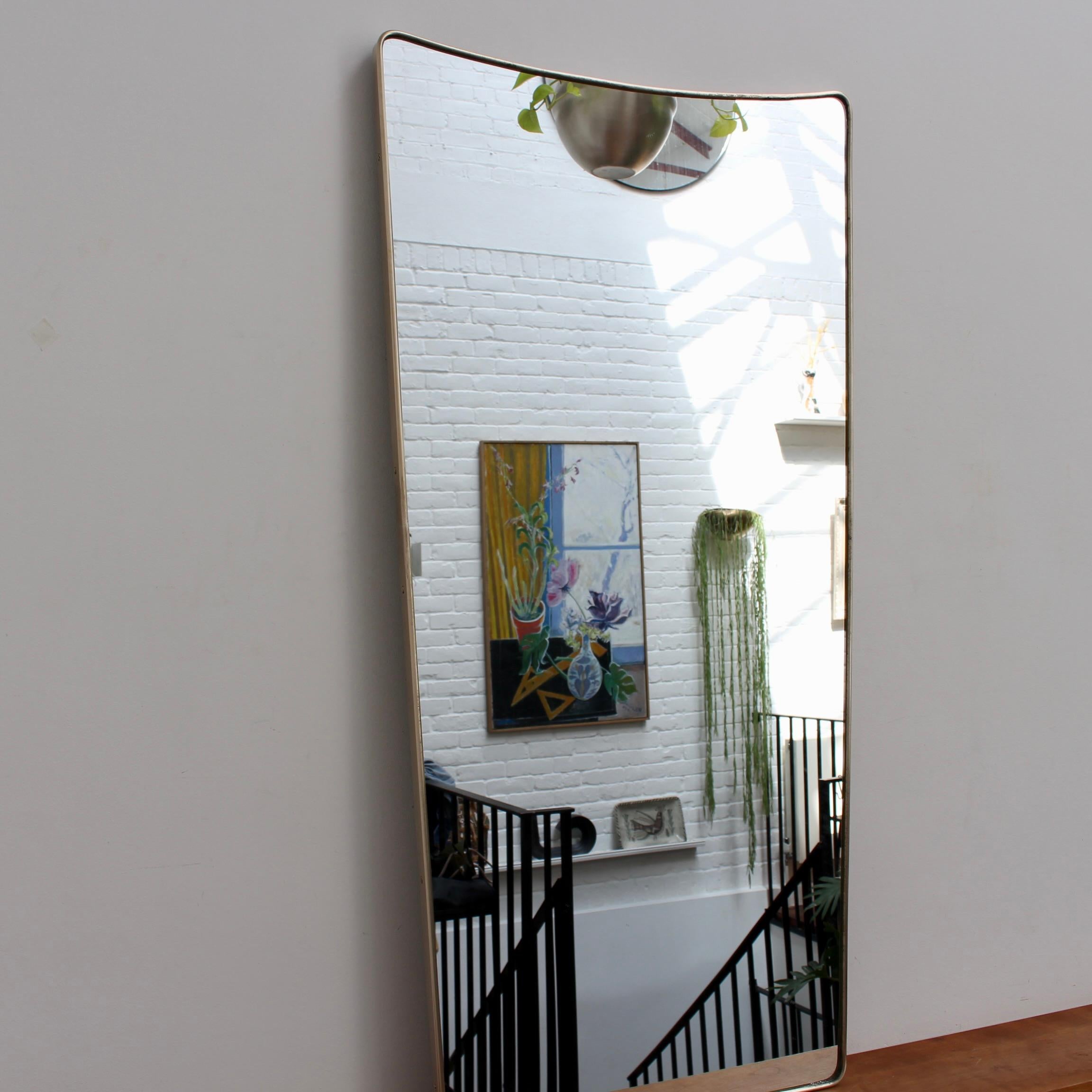 Italienischer Wandspiegel aus der Mitte des Jahrhunderts mit Messingrahmen (ca. 1950). Der große Spiegel ist klassisch geformt und zeichnet sich durch einen modernen Stil aus. Der Messingrahmen weist eine schöne, gealterte Patina auf, obwohl er erst