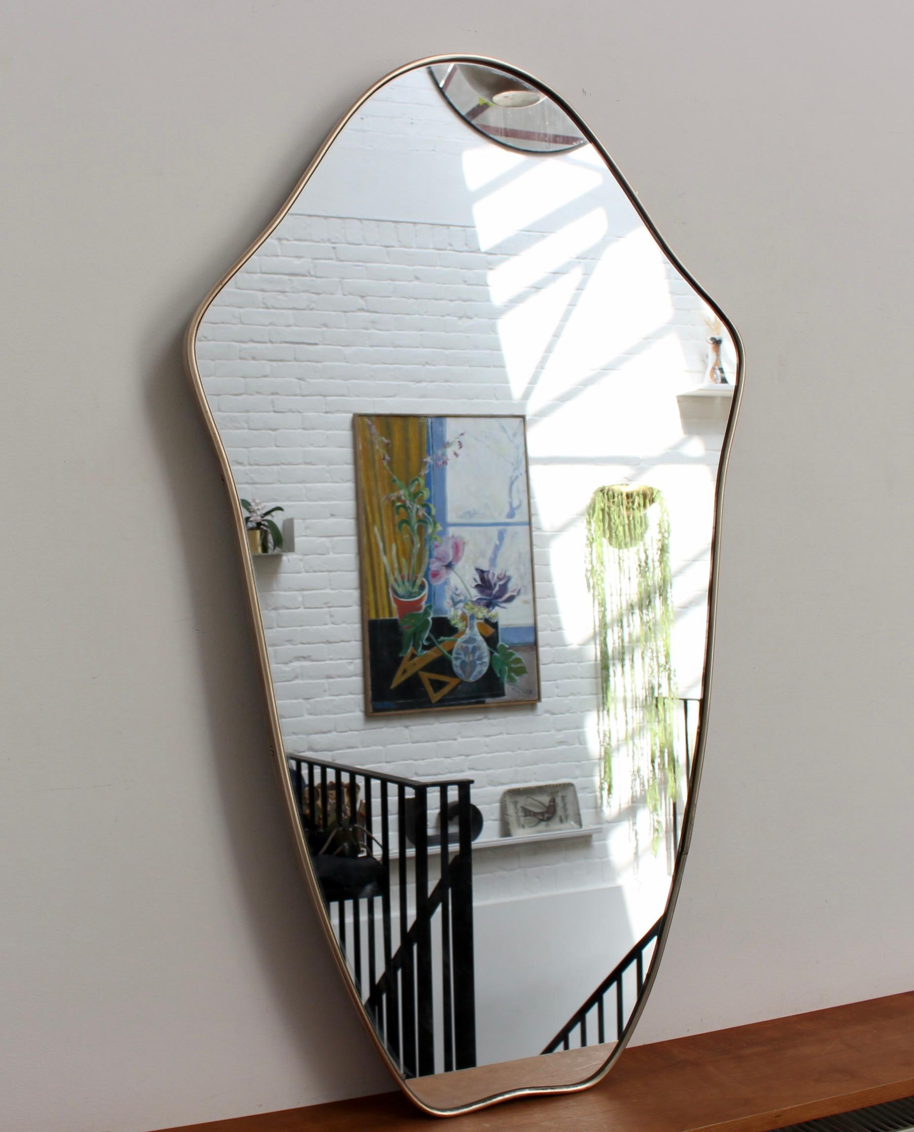 Midcentury Italian wall mirror with brass frame (circa 1950s). The mirror is classically-shaped and distinctive in a Modern style. A beautiful patina develops on the brass frame - this one has been recently polished. There is a sturdy backing