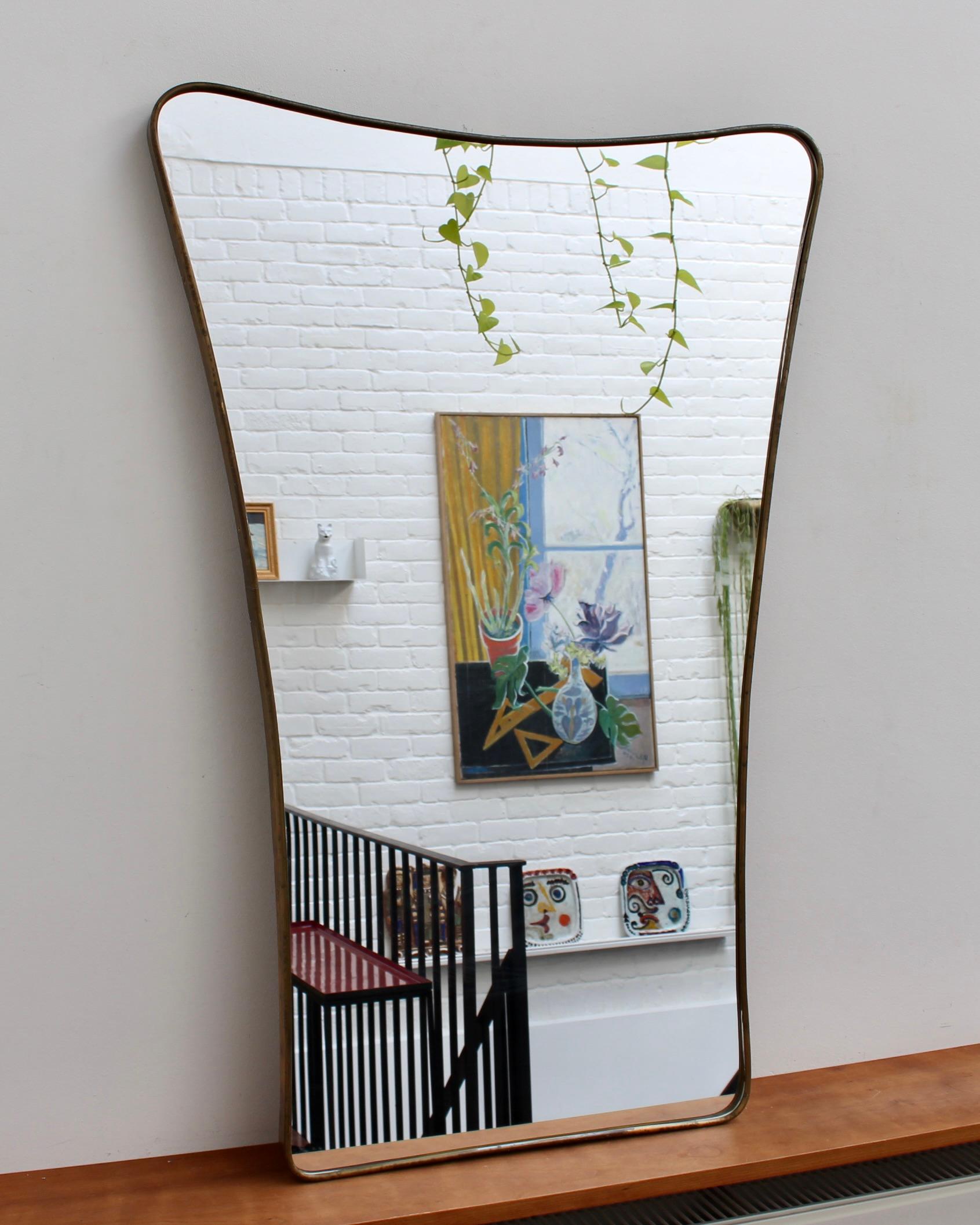 Italienischer Wandspiegel aus der Mitte des Jahrhunderts mit Messingrahmen (ca. 1950). Der Spiegel ist klassisch geformt und zeichnet sich durch einen modernen Stil aus. Es ist insgesamt in gutem Zustand. Auf dem Messingrahmen entwickelt sich eine