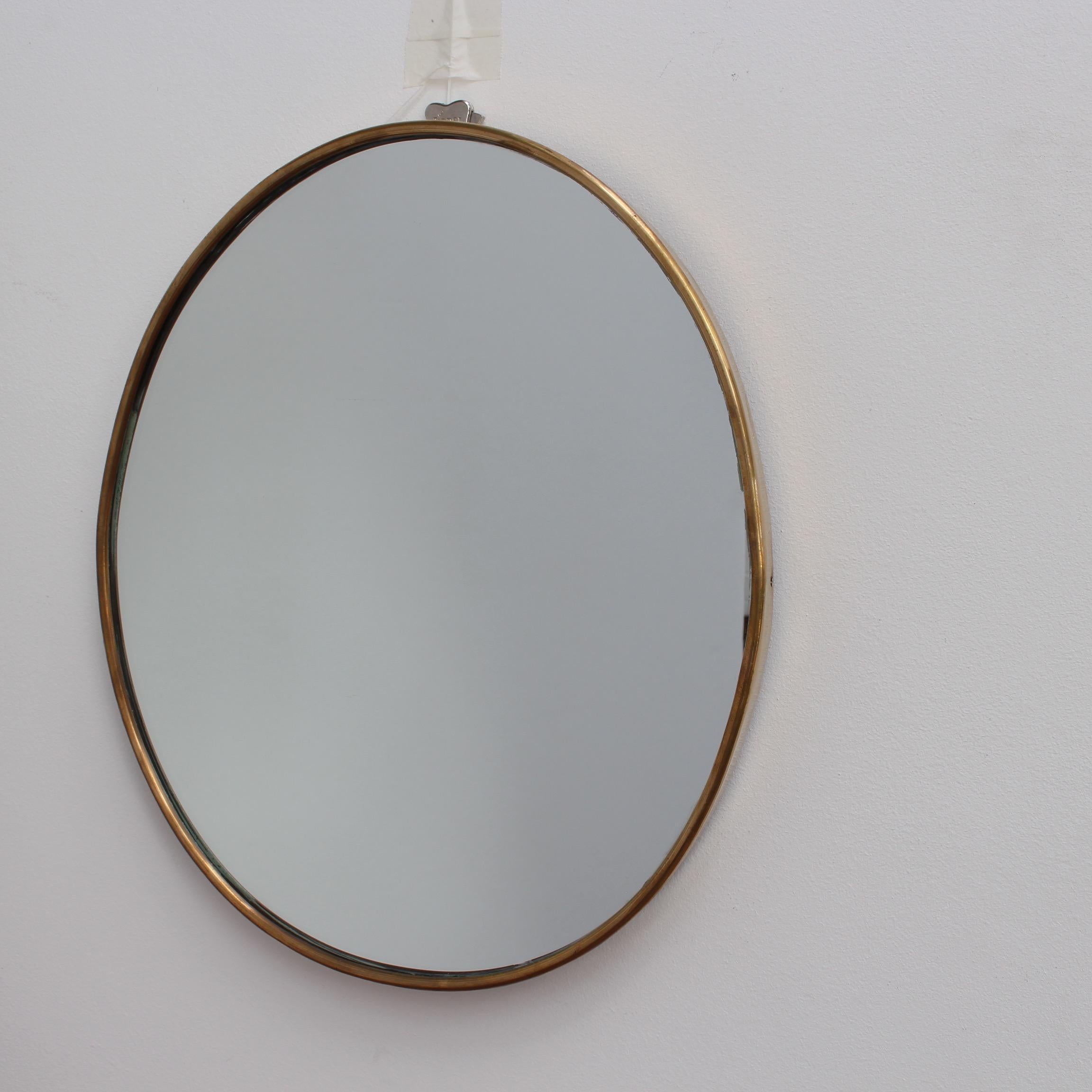 Small-scale midcentury Italian wall mirror with brass frame (circa 1950s). The mirror is porthole-shaped with sensuous curves. It is classically elegant and distinctive in a modern Gio Ponti style in good vintage condition. As seen in the