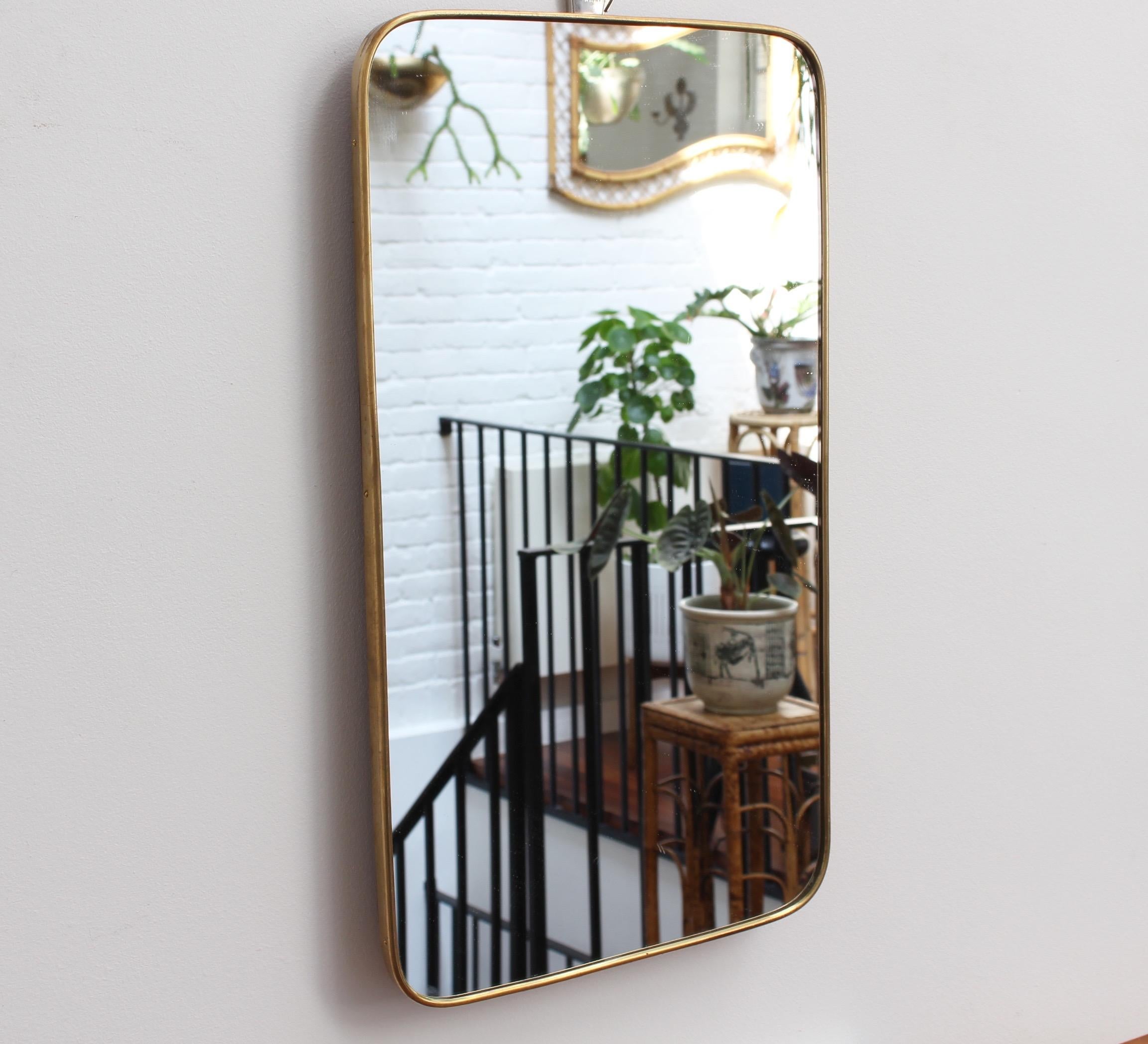Small scale midcentury Italian wall mirror with brass frame, circa 1950s. The mirror is rectangular with sensuously curved edges. It is classically elegant and distinctive in a modern Gio Ponti style. Fittings are in place to allow it to be hung