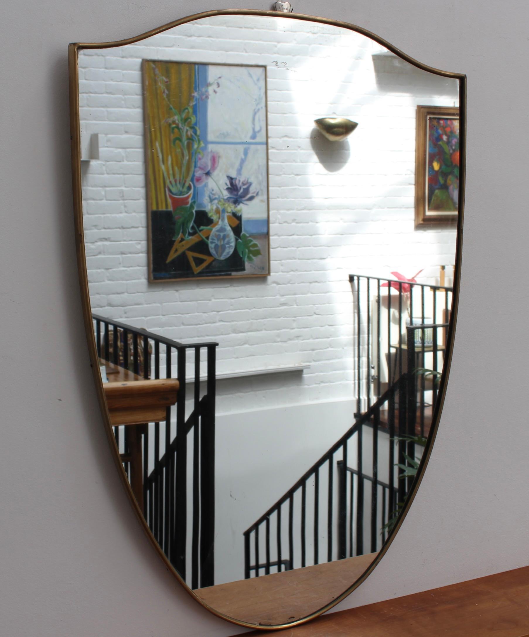 Miroir mural italien vintage avec cadre en laiton (circa 1960s). Le miroir a une forme magnifique et une élégance classique dans le style moderne de Gio Ponti. Le cadre est en bon état général, avec une patine vieillie ; il y a quelques taches