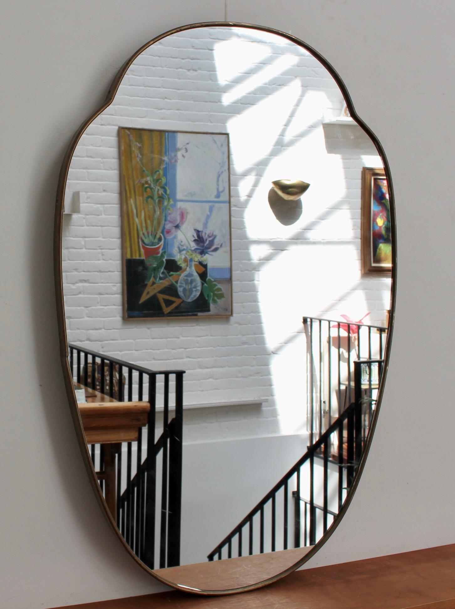 Mid-century Italian wall mirror with brass frame (circa 1960s). The mirror is classically-shaped and distinctive in a Modern style. It is in good overall condition. A beautiful patina has developed on the brass frame. The mirror glass has minor