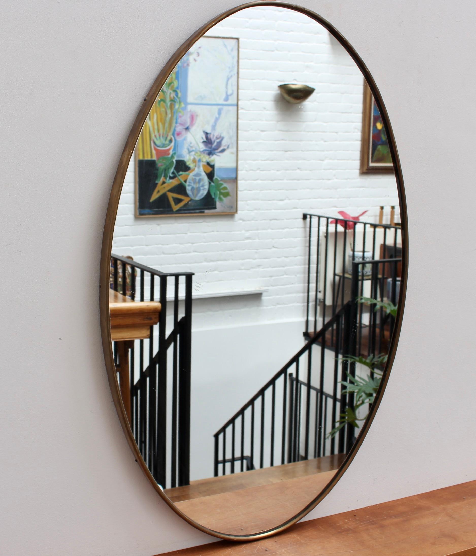 Mid-century Italian wall mirror with brass frame (circa 1960s). The mirror is oval-shaped and distinctive in a Modern style. It is in good overall condition. A beautiful patina has developed on the brass frame. There are some minor blemishes on the