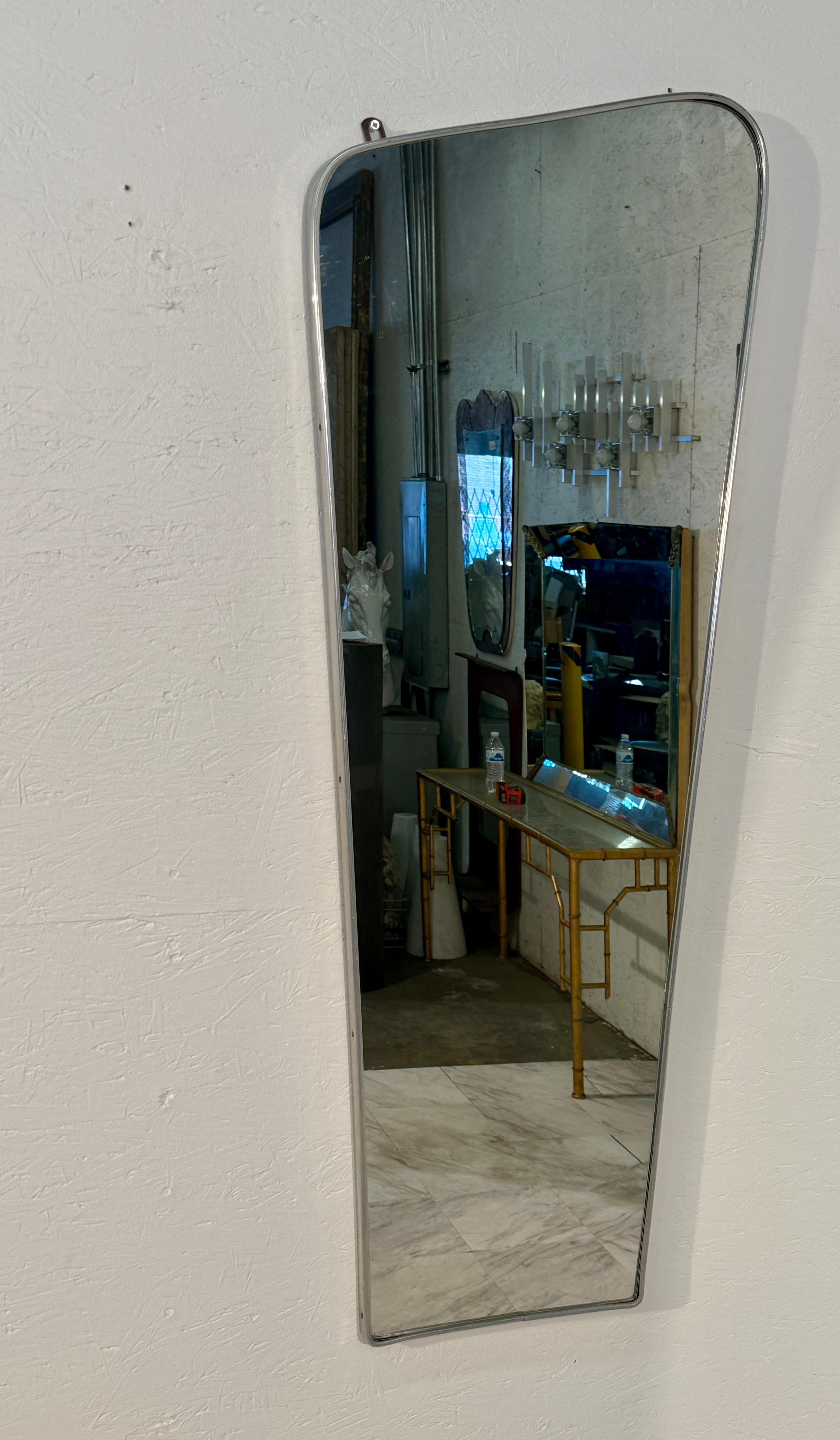 Elegant miroir mural italien du milieu du siècle dernier, datant des années 1960, présentant une forme trapézoïdale asymétrique distinctive qui ajoute une touche dynamique à tout espace. Le miroir est encadré de chrome épuré, ce qui lui confère un
