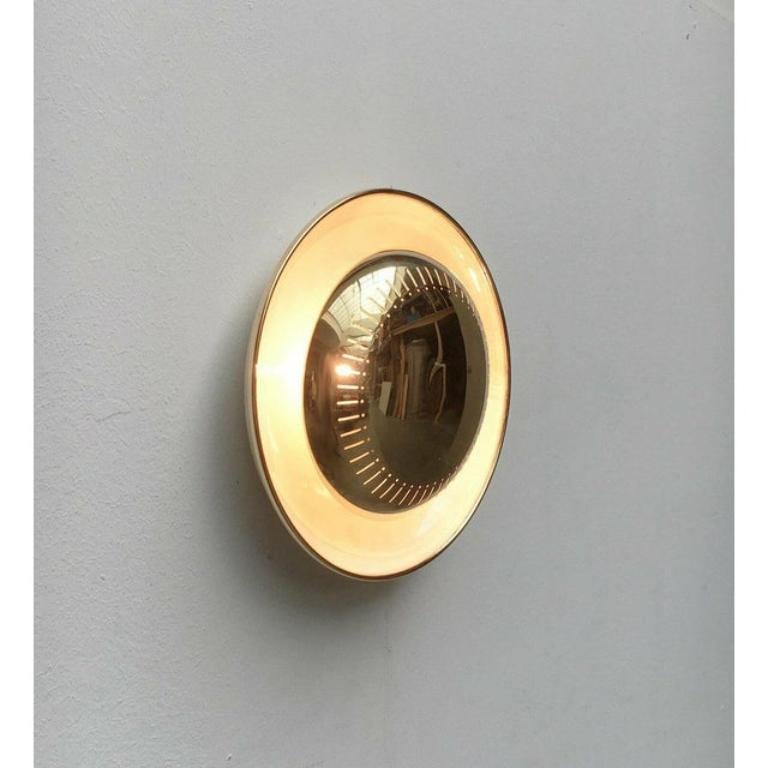 Imposing Mid-Century wall lamp.

The lamp consists of two parts. The curved reflector trough and the shiny front element. The front shields the light source and protects against glare. The light emerges indirectly and is reflected by the gentle
