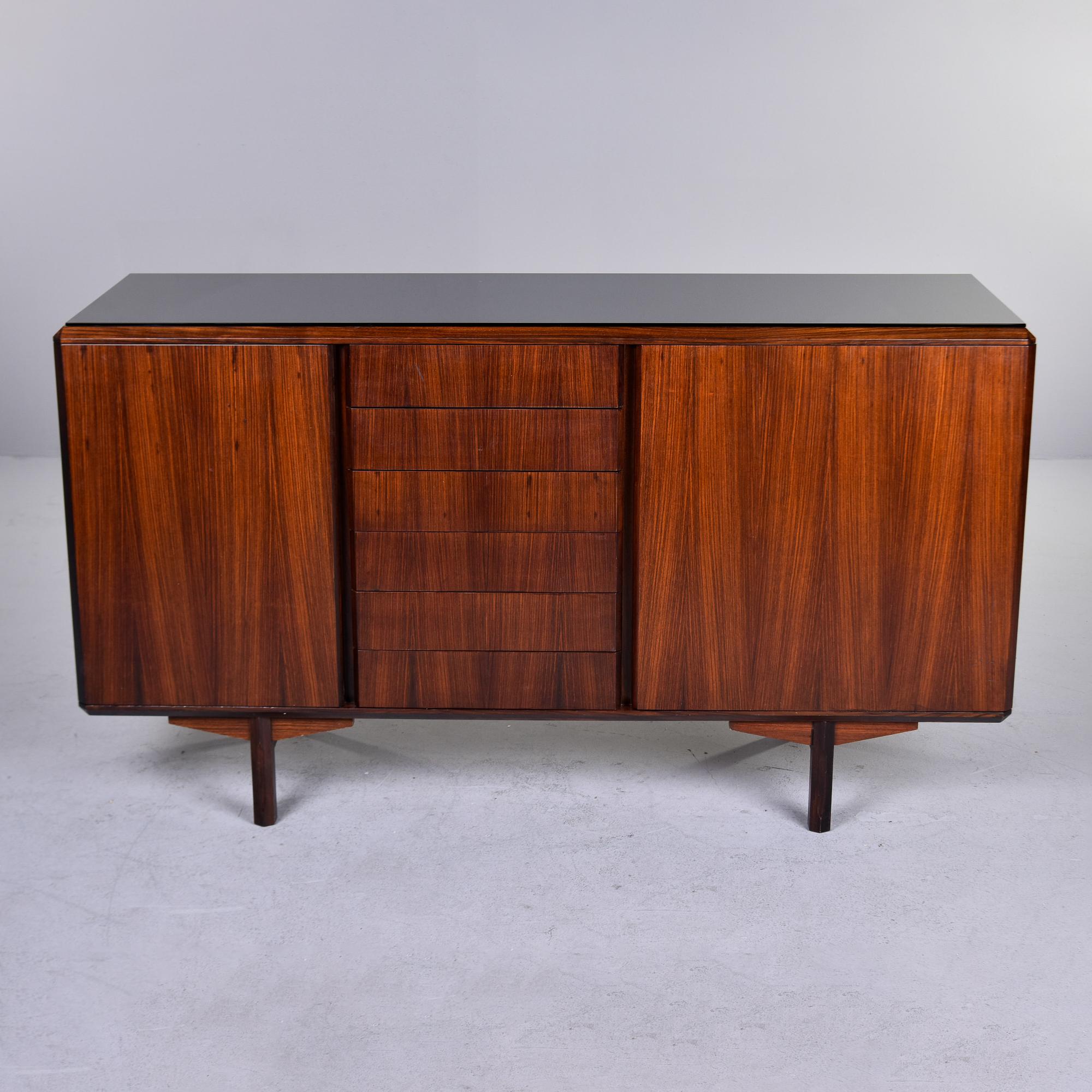 Found in Italy, this circa 1960s cabinet has a distinct mid century shape and nicely figured walnut. This is a practical and versatile cabinet. Six functional center drawers are flanked by side compartments with hinged doors and a single interior