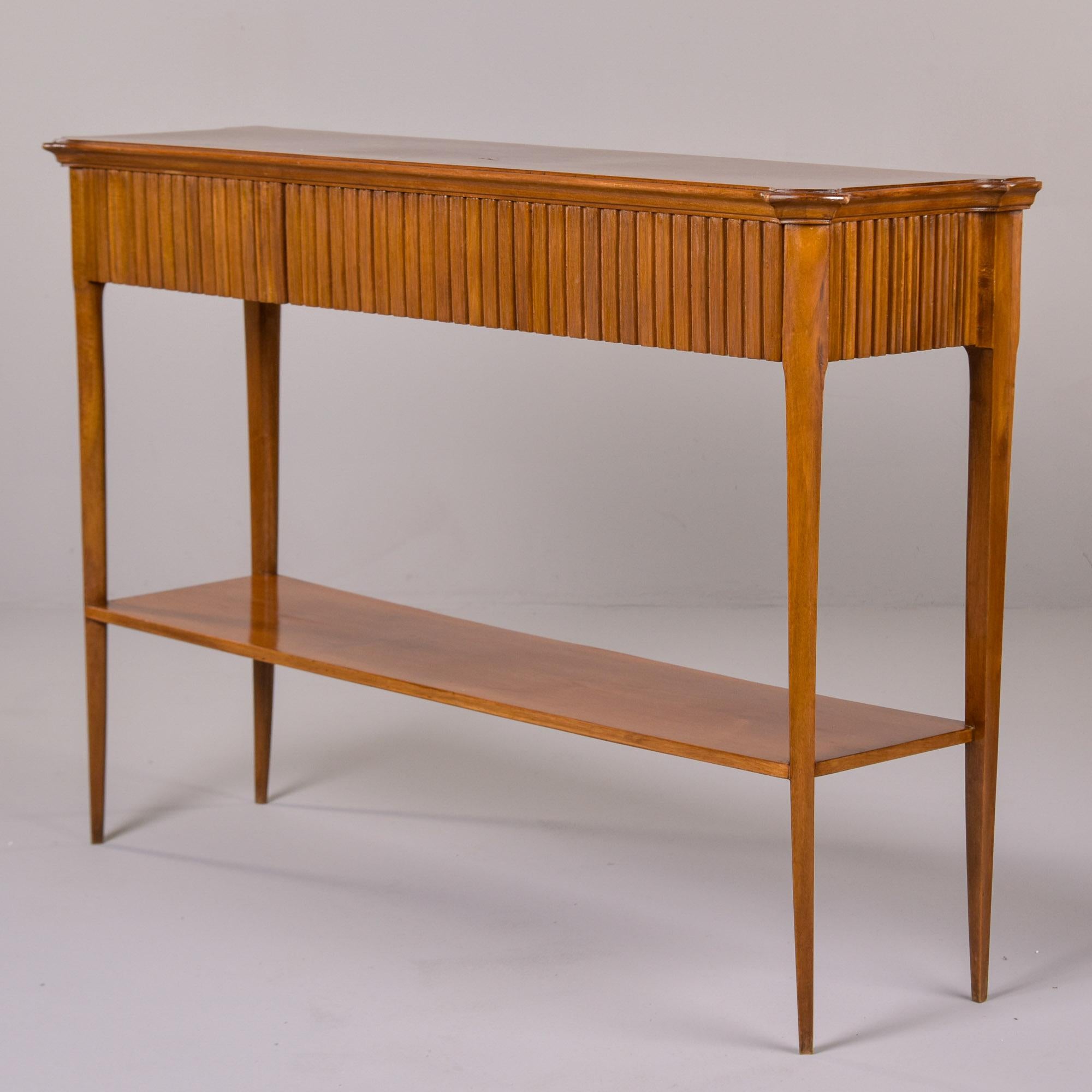 Found in Italy, this walnut console dates from the 1960s. This table features reeded apron and sides, tapered legs and a bottom shelf. This console has a single center drawer which is divided into three sections. Unknown Italian maker. Very good