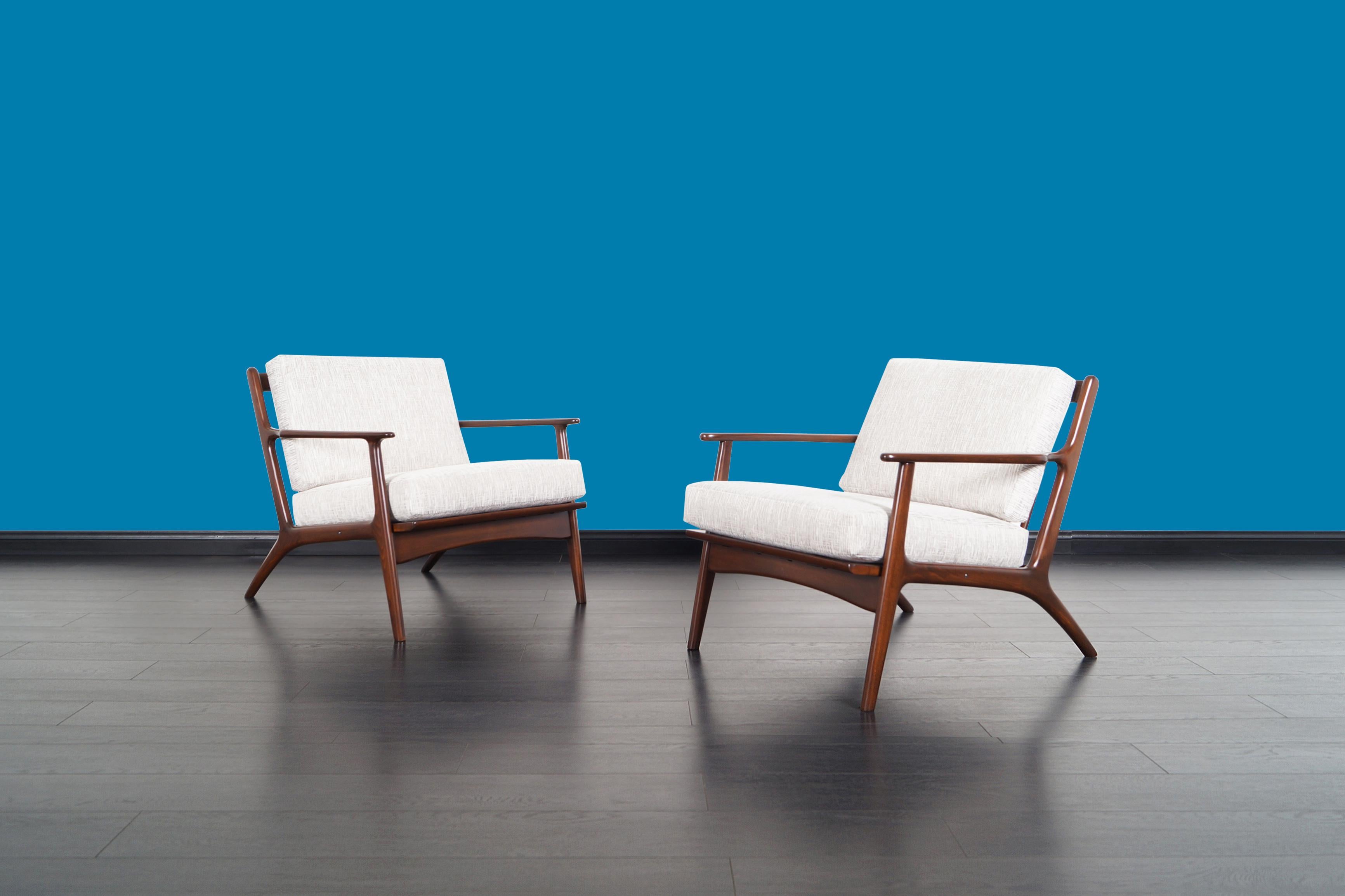 Spectacular pair of vintage lounge chairs designed and manufactured in Italy, circa 1950s. These elegant lounge chairs feature a solid walnut stained beech frame with sculptural armrests and slatted backrest, assuring a sleek profile view from all