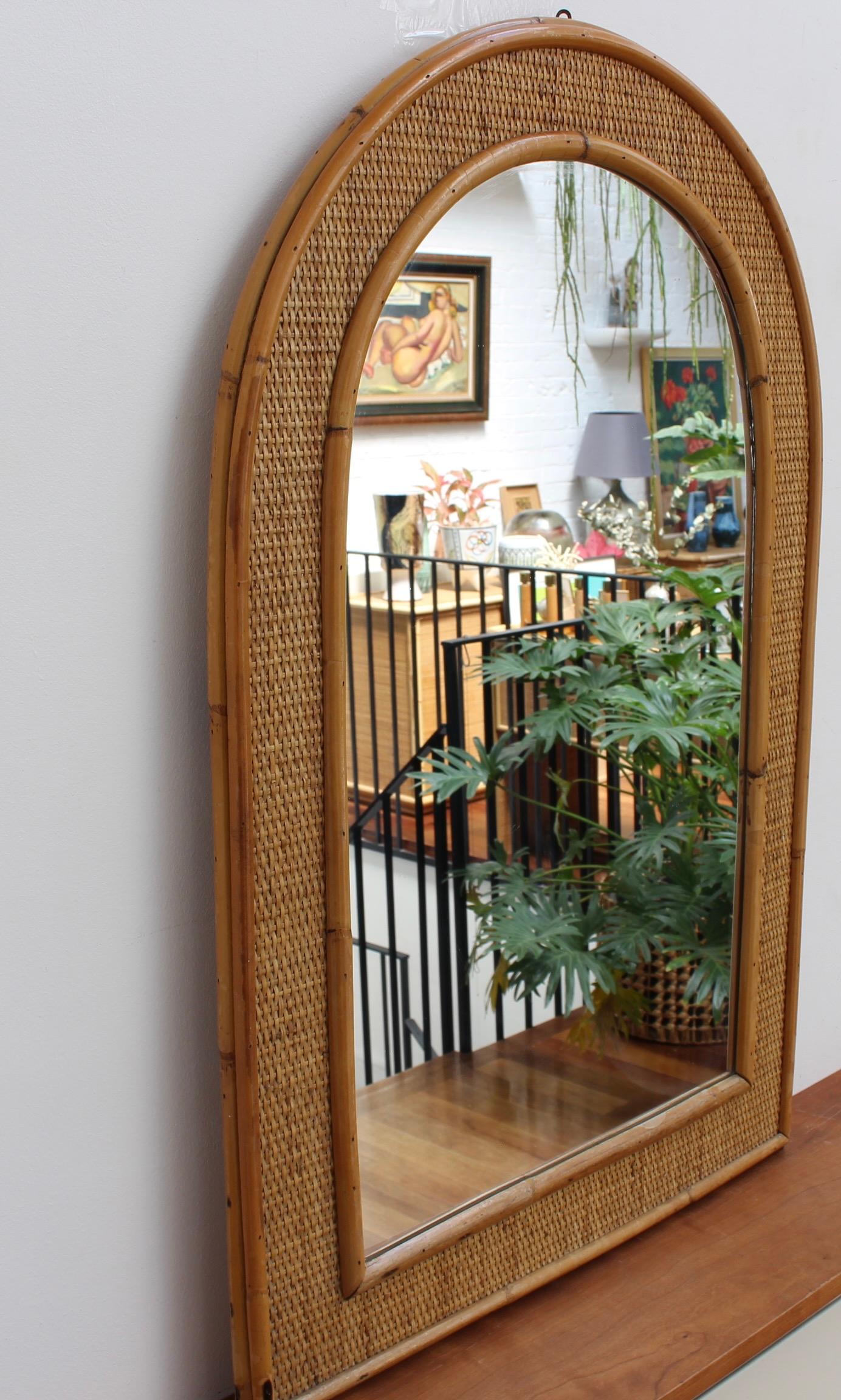 Mid-century Italian wicker and rattan wall mirror (circa 1960s). This piece has a delightful arched shape with glass enclosed by the caned frame which is itself, framed by wicker and more cane. The wicker In between the two frames adds texture and