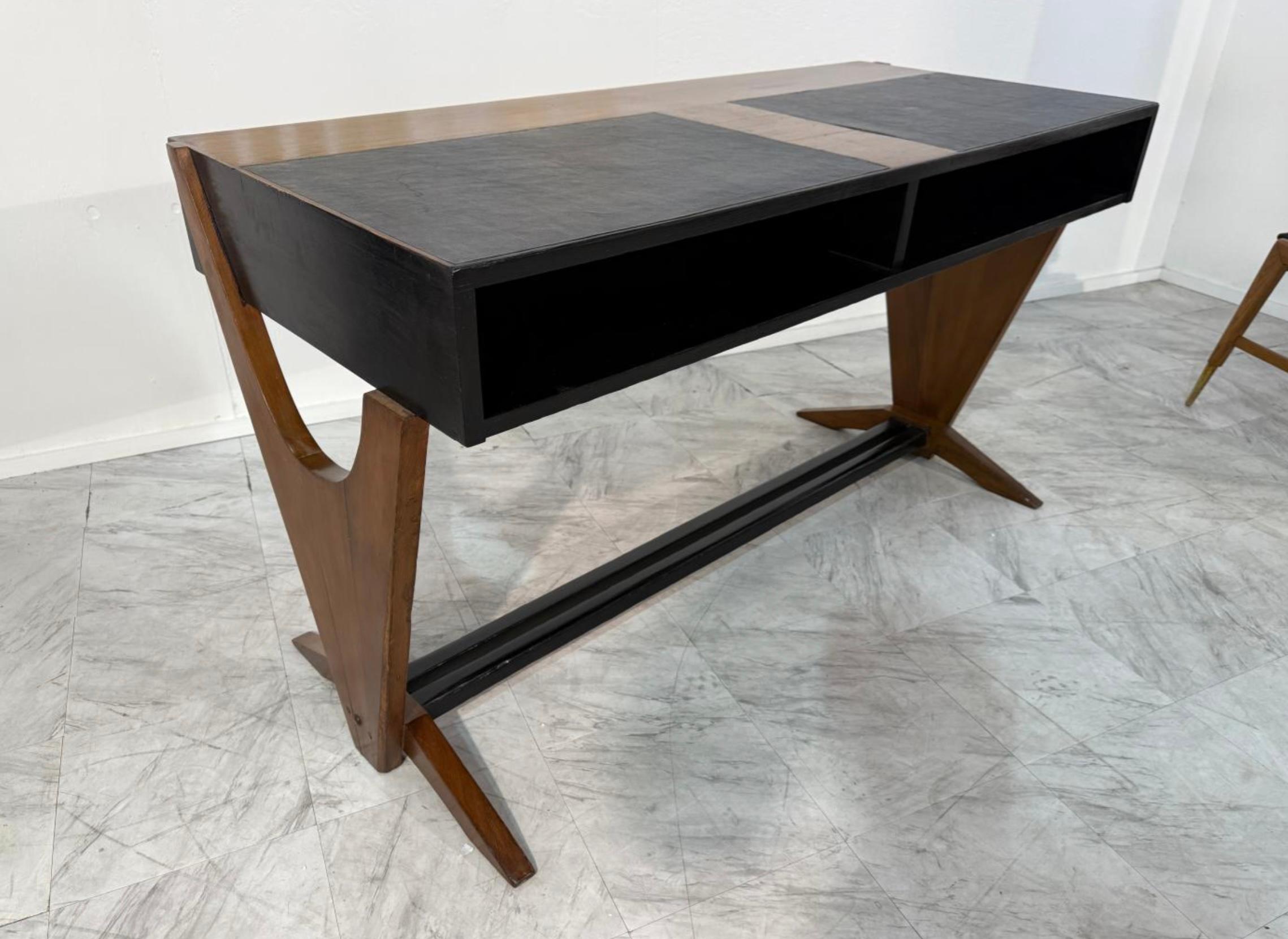 El escritorio presenta la mezcla característica de Buffa de forma arquitectónica y artesanía refinada. Presenta una elegante tapa rectangular en un acabado bicolor que contrasta: la madera natural flanquea una sección central en negro, posiblemente