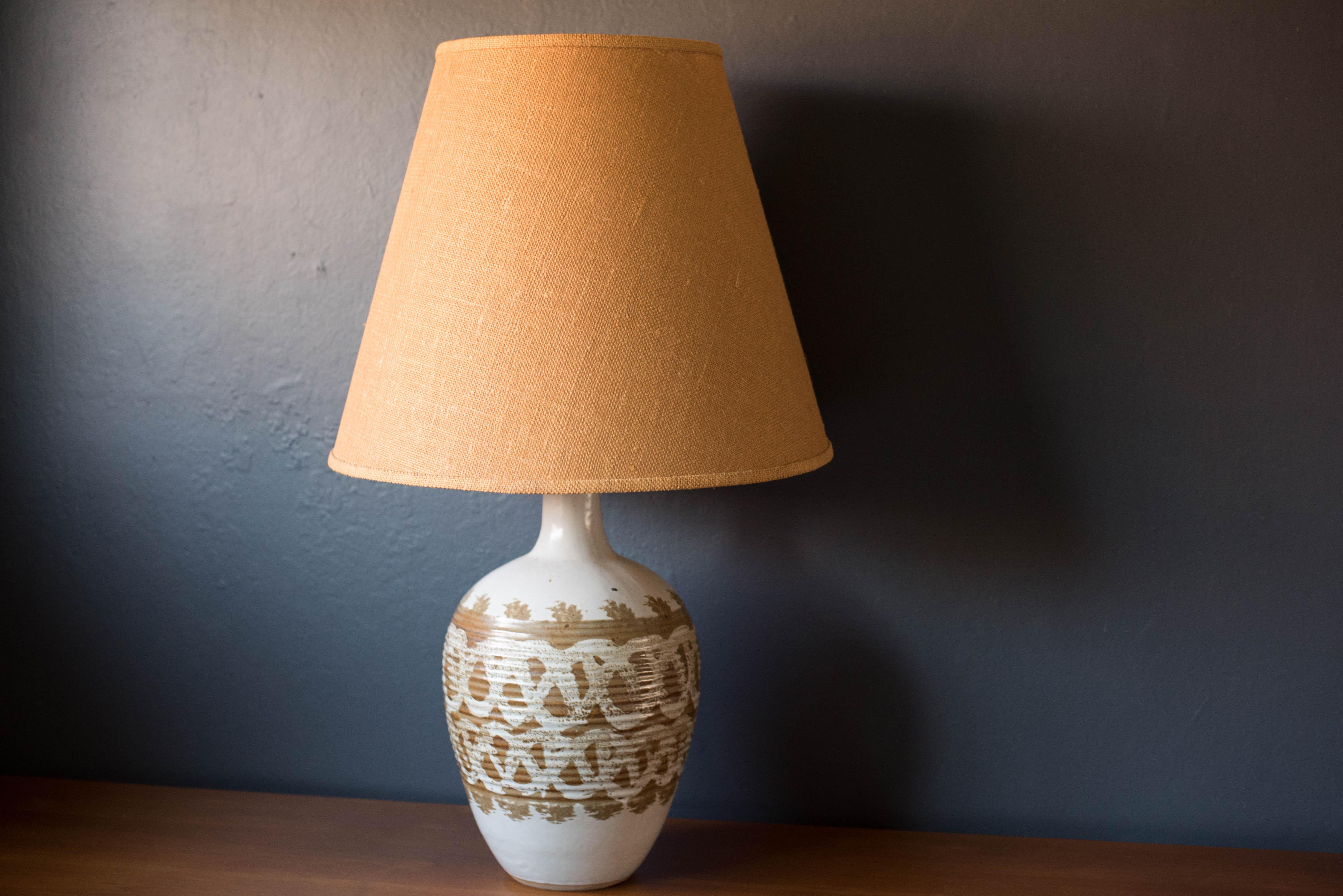 Vintage 1970s ceramic table lamp accented with a textural natural earth tone design. This piece features a heavy bulbed base that is glazed in a glossy ivory finish. Equipped with a three way switch to emit a soft glow or brighter light if desired.