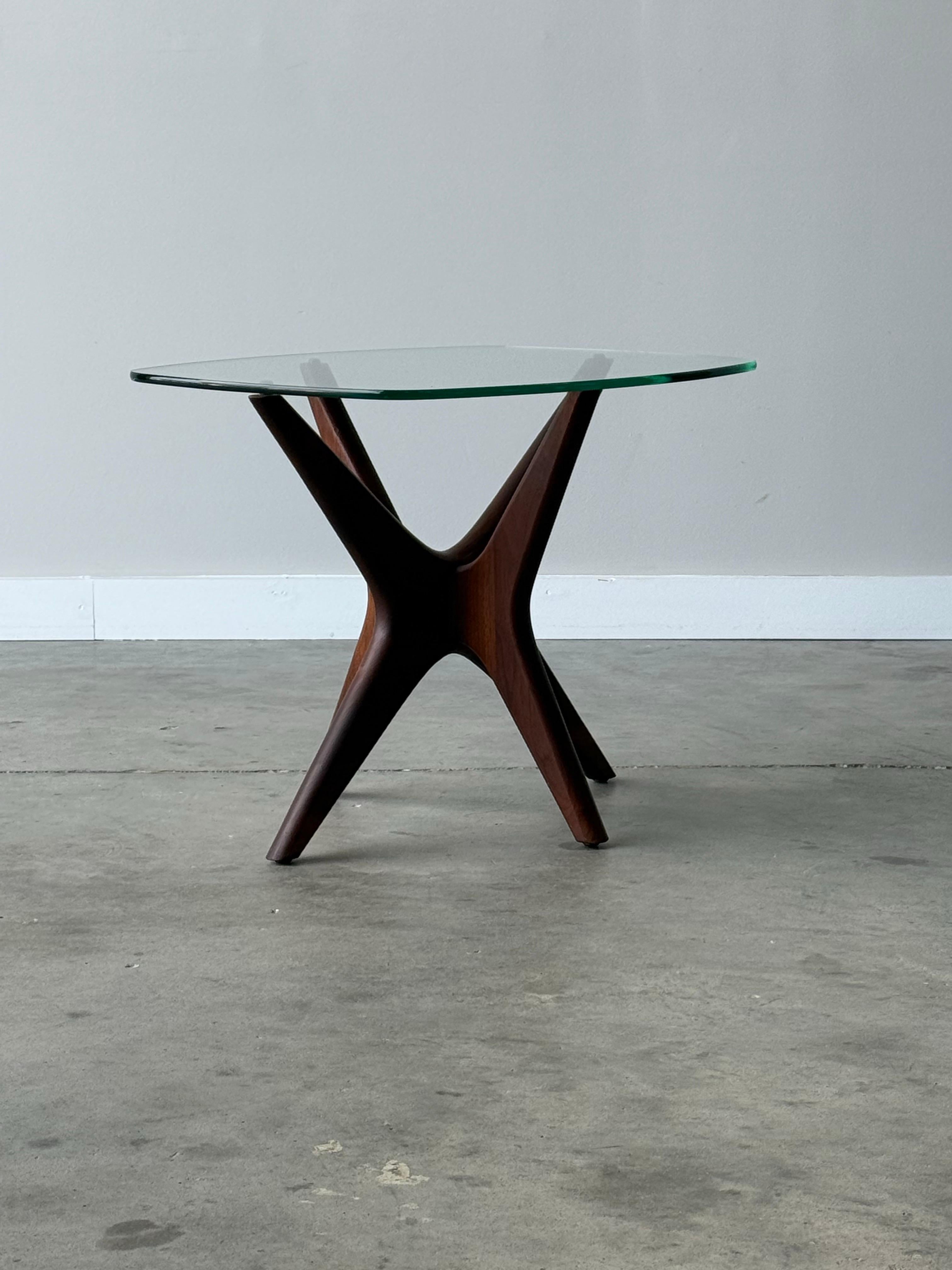 Mid-century “Jacks” side table designed by Adrian Pearsall, made circa 1960s. This particular piece features a sleek, rectangular glass top that rests gracefully on a sculptural walnut wooden base, warm in tone. 

The wooden base is inspired by