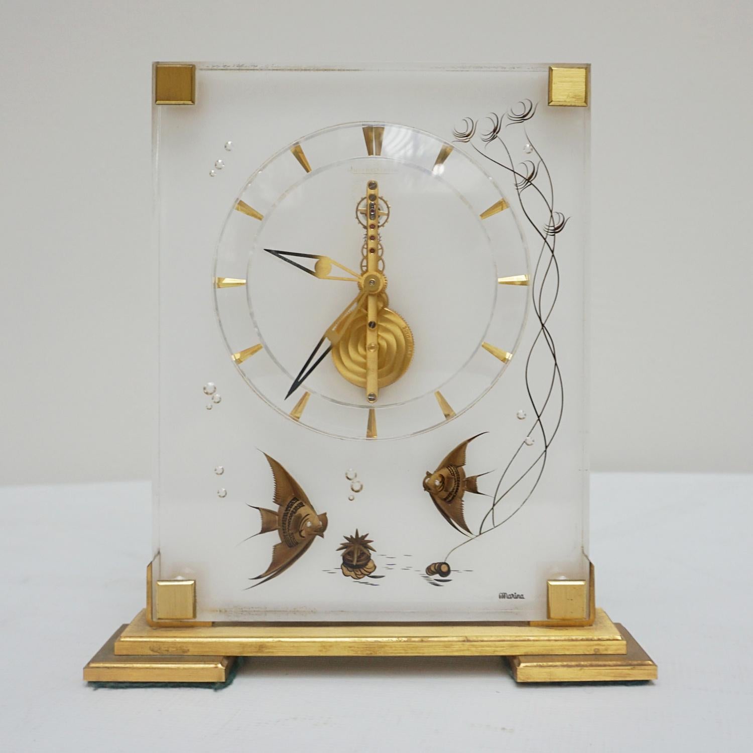 A Mid-Century Jaeger-LeCoultre mantel clock in a Lucite case with inset brass decoration showing fish with reeds and air bubbles rising.. Eight day movement by Jaeger-LeCoultre with baton numerals and original gilded hands. Marina inset to lower