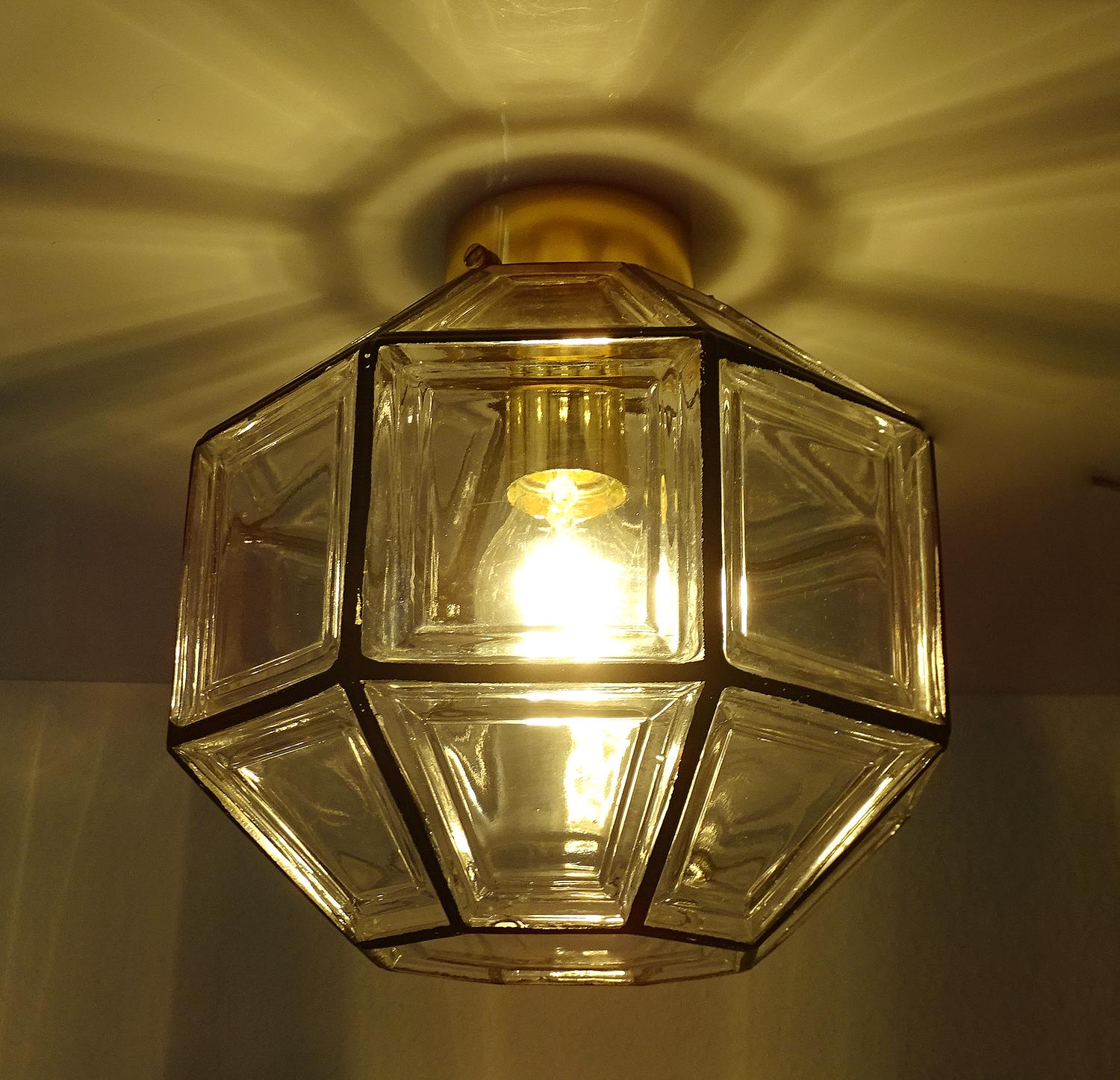 Flush mount light fixture by Hans-Agne Jakobsson AB, featuring a polyhedral glass shade encased in an coated iron style grid reminiscent of antique lanterns, polished brass base. The design was featured in the Hans-Agne Jakobsson AB Catalog under