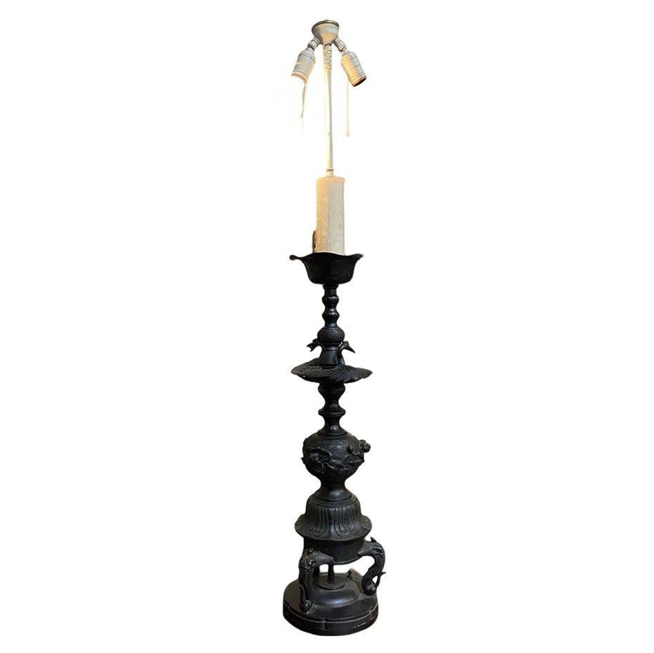 Mid-century sculptural fusion bronze table lamp features a classic Western candle stick design with a Chinese motif featuring cranes, foo dogs, and a floral design along the center. The lamp is comprised of casted bronze parts that have been fixed