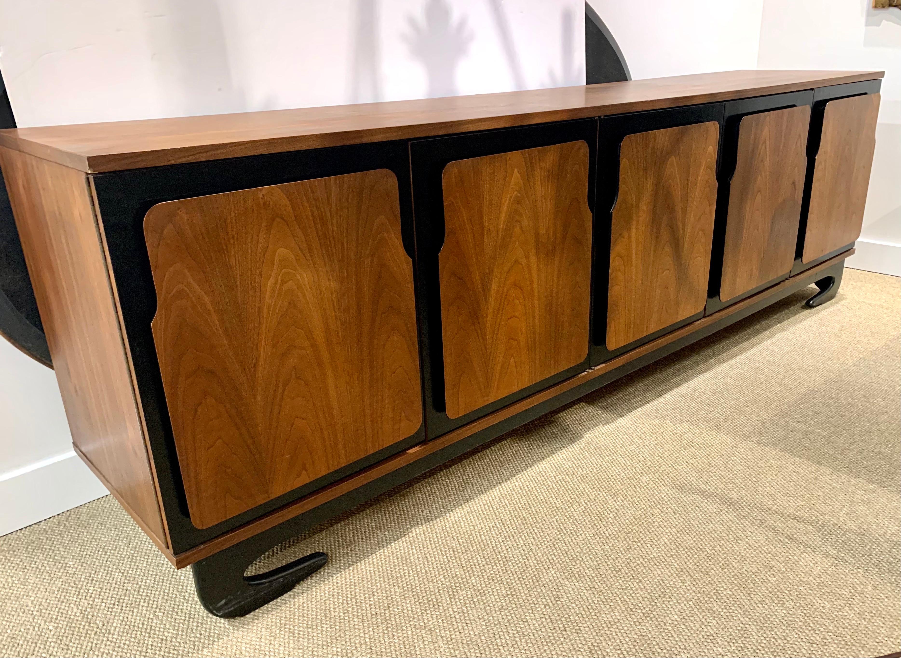 Mid century extra long walnut dresser with five shaped doors on a black lacquered base. Four left doors open to storage with holes for adjustable shelving. Right door opens to two drawers. Shelves not included. This is in beautiful vintage condition