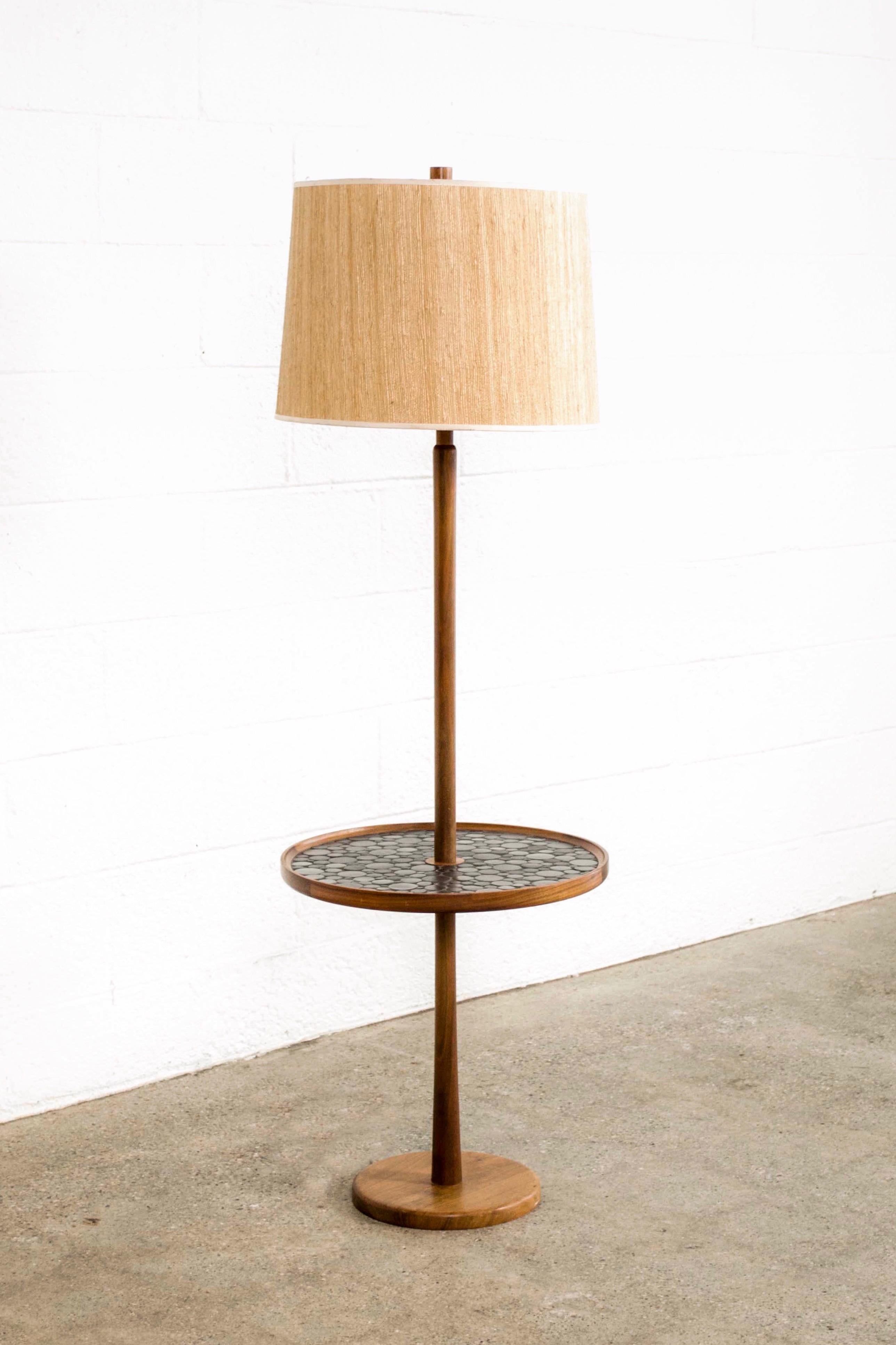 This vintage midcentury floor lamp with integrated table was designed by Jane and Gordon Martz circa 1960. The Classic design features a round inlaid mosaic table with round dark slate gray ceramic tiles of varying sizes. The long solid walnut stem