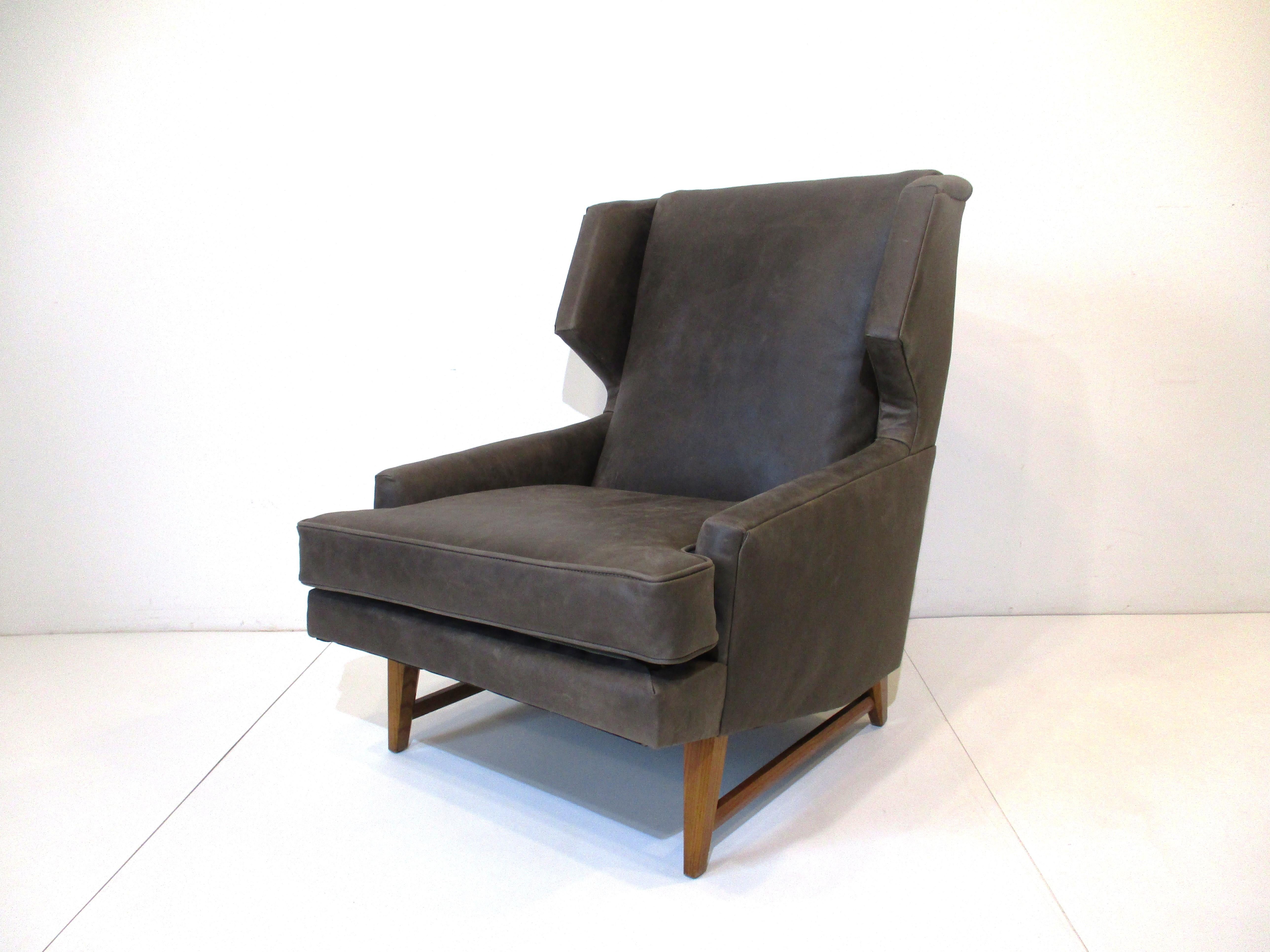 A midcentury wingback styled lounge chair restored in a distressed natural grige colored soft leather. The wood legs and strechers have beveled details giving the chair a nice tailored look mixing with the distressed warm leather. Designed in the
