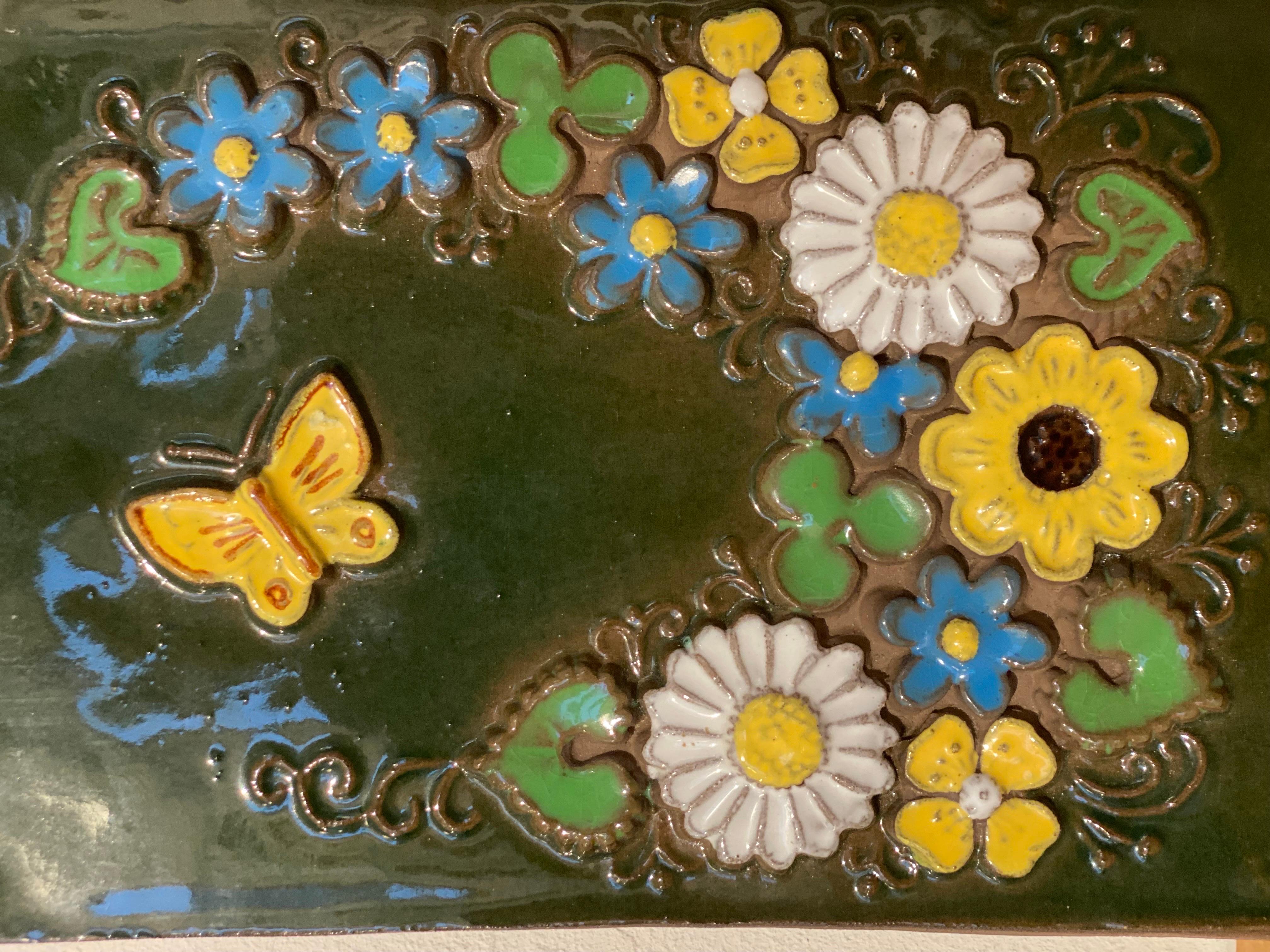 Mid-Century Swedish ceramic floral wall plaque by Jie Gantofta Sweden. Created by designer Aimo Nietosvuori.
This ceramic tile with natural flowers and butterfly is hand-painted in vibrant mauve, canary yellow, navy blue, green and white tones.