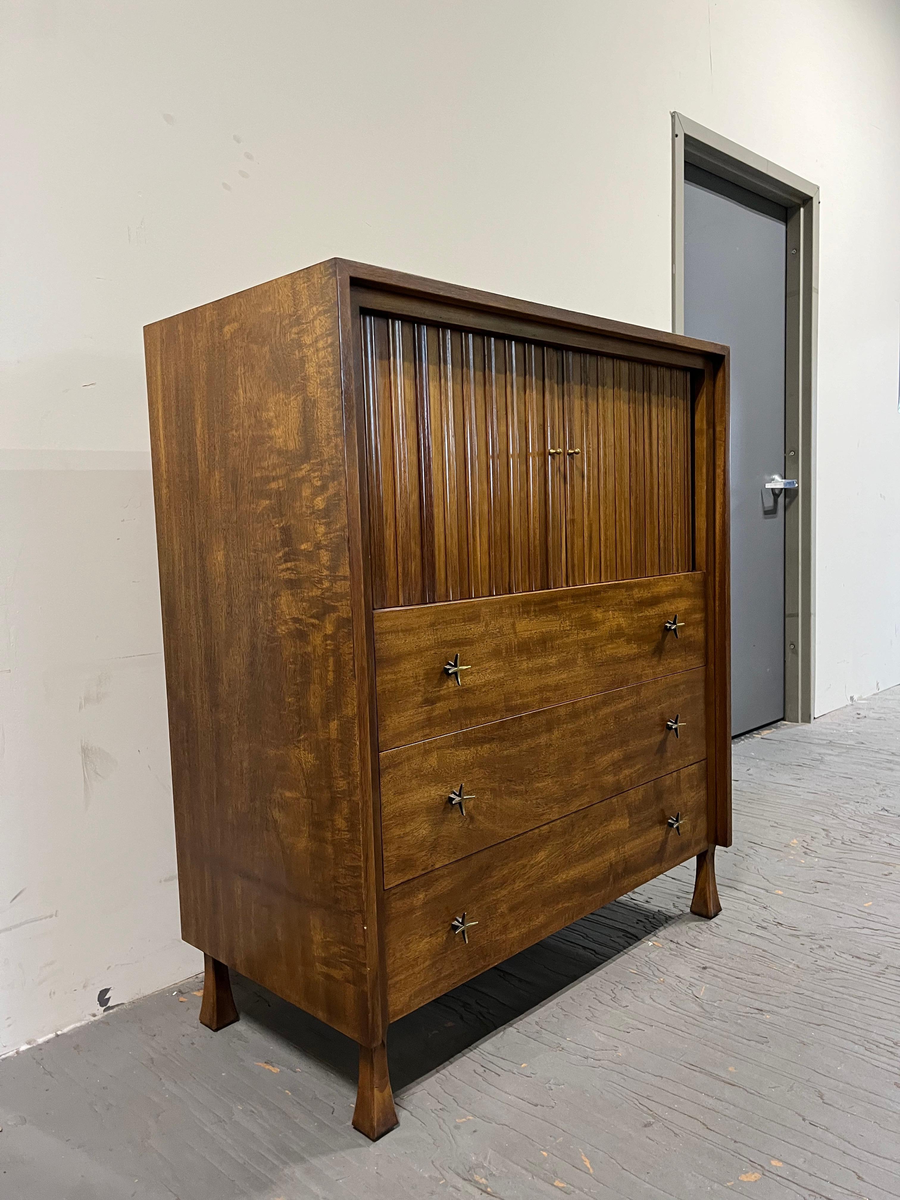 Mid Century tall dresser with tambour doors that conceal several cubbies and one small drawer. Fantastic design with brutalist detail with great stylish drawer pulls with star design. John Stuart for John Widdicomb. 
Curbside to NYC/Philly $550