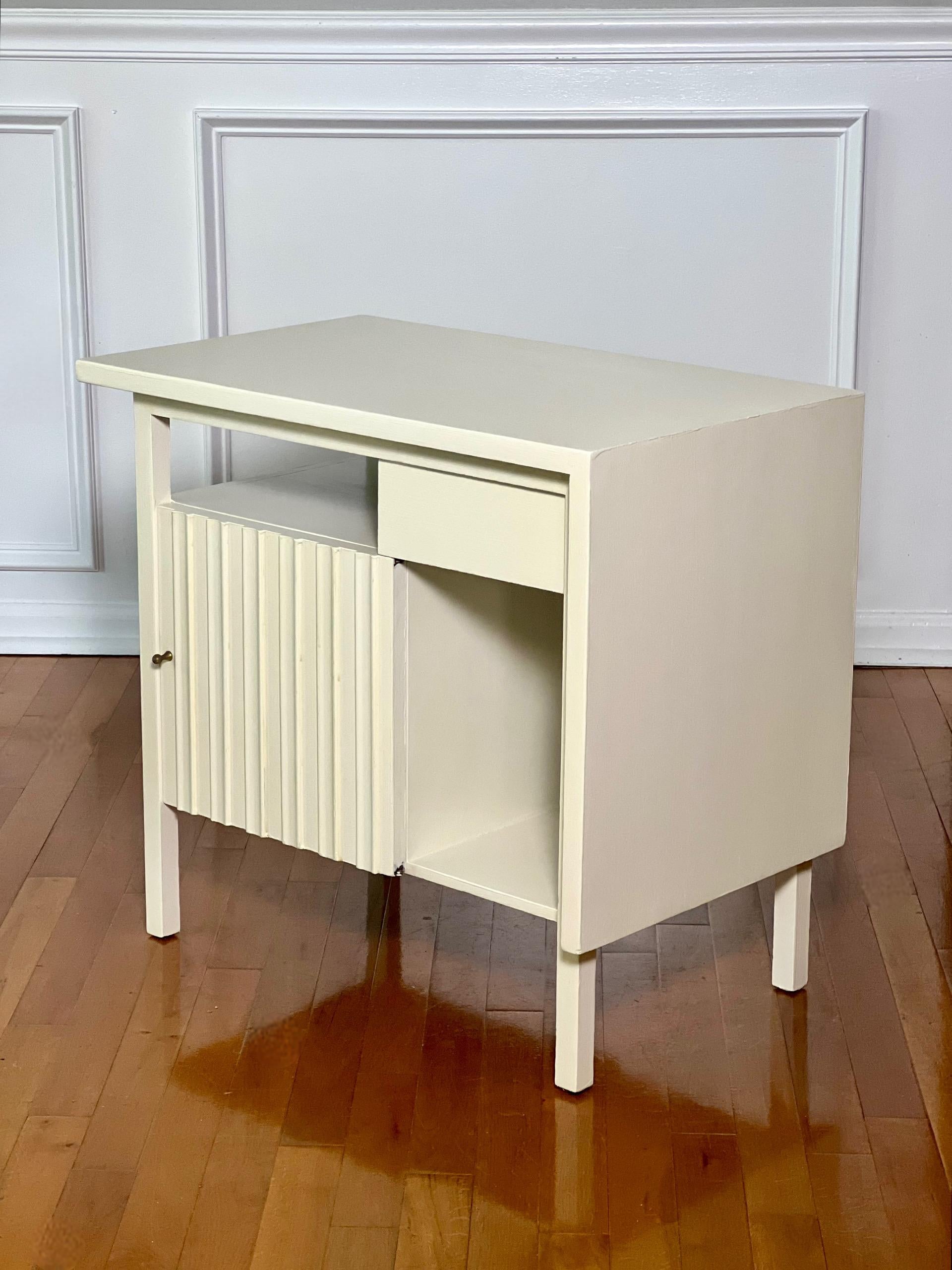 Vintage mid century nightstand or side table by John Widdicomb, refinished in white, c. 1950s.

Great stand with sleek lines featuring a cabinet behind a sculpted door with a diminutive brass knob and a single drawer.  A very smart design on this