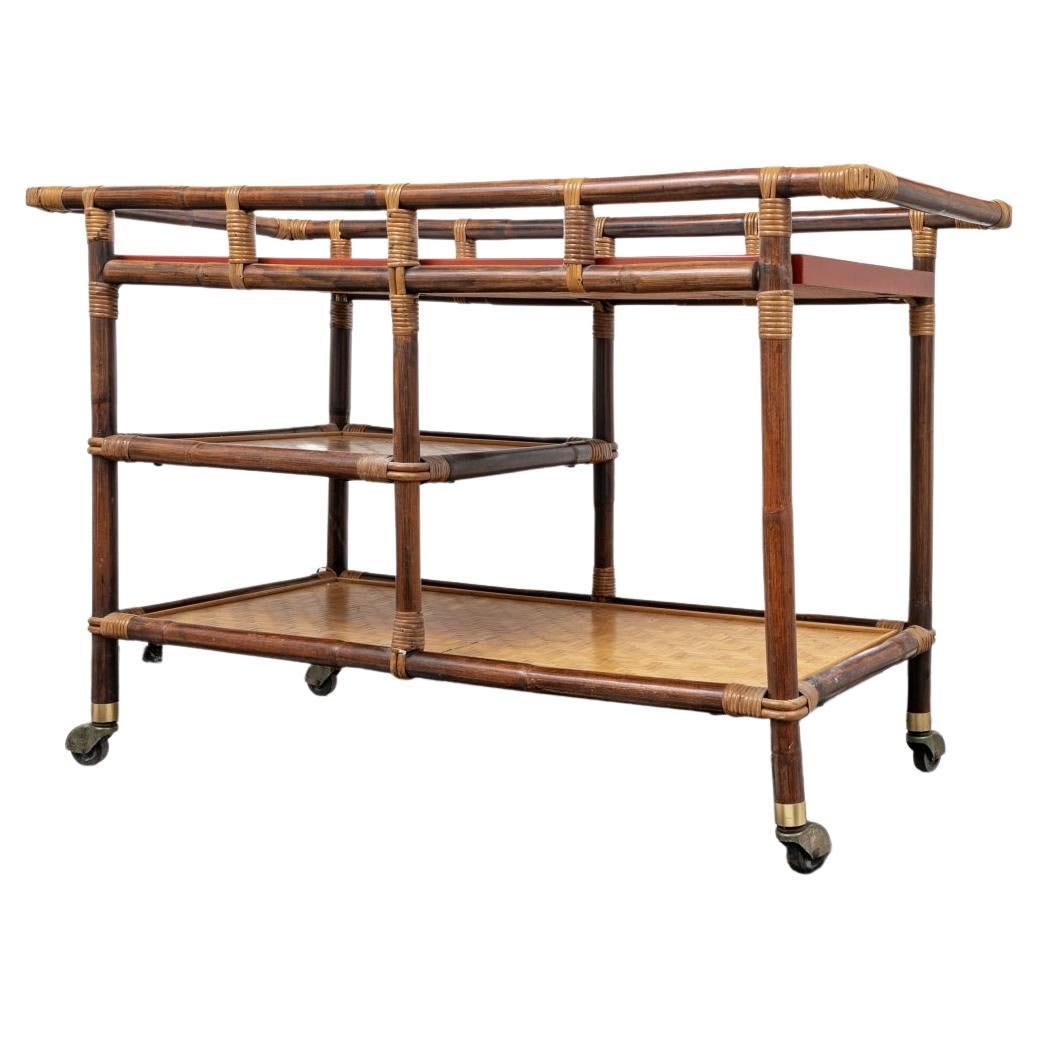 Classic 1960’s Mid Century design with Stained Rattan Frame, Tile inlaid Top with Stylish Asian Characters framed by Cinnabar framing, Lower Shelves clad in Geometric Patterned Bamboo, Split Rattan Wrappings, Castors and Brass Clad Leg Caps. The