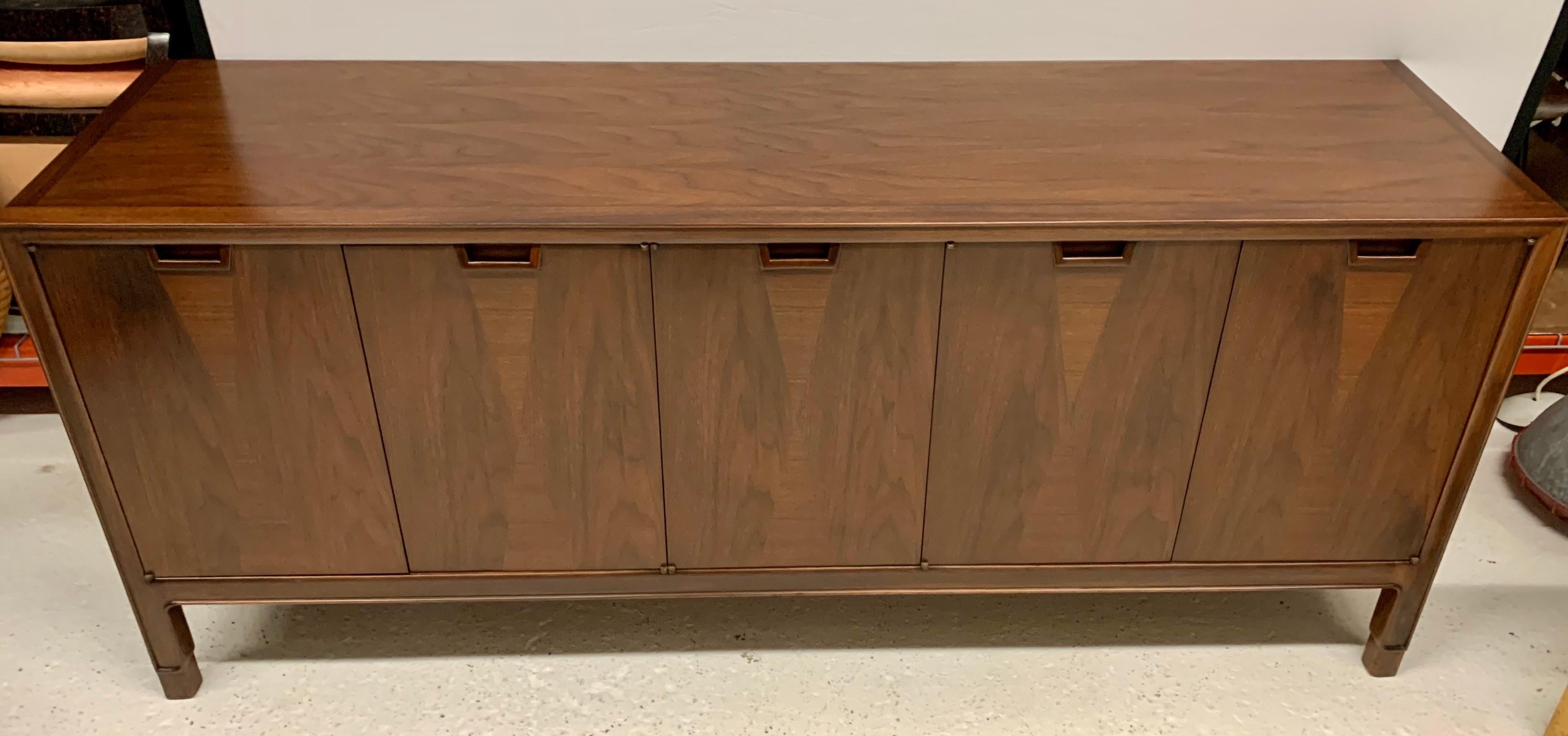Beautifully restored John Stuart for Janus Collection midcentury credenza features beautiful walnut graining accented by hourglass shaped alternating veneers. There are five doors; the two left doors open to three drawers. The right three doors open