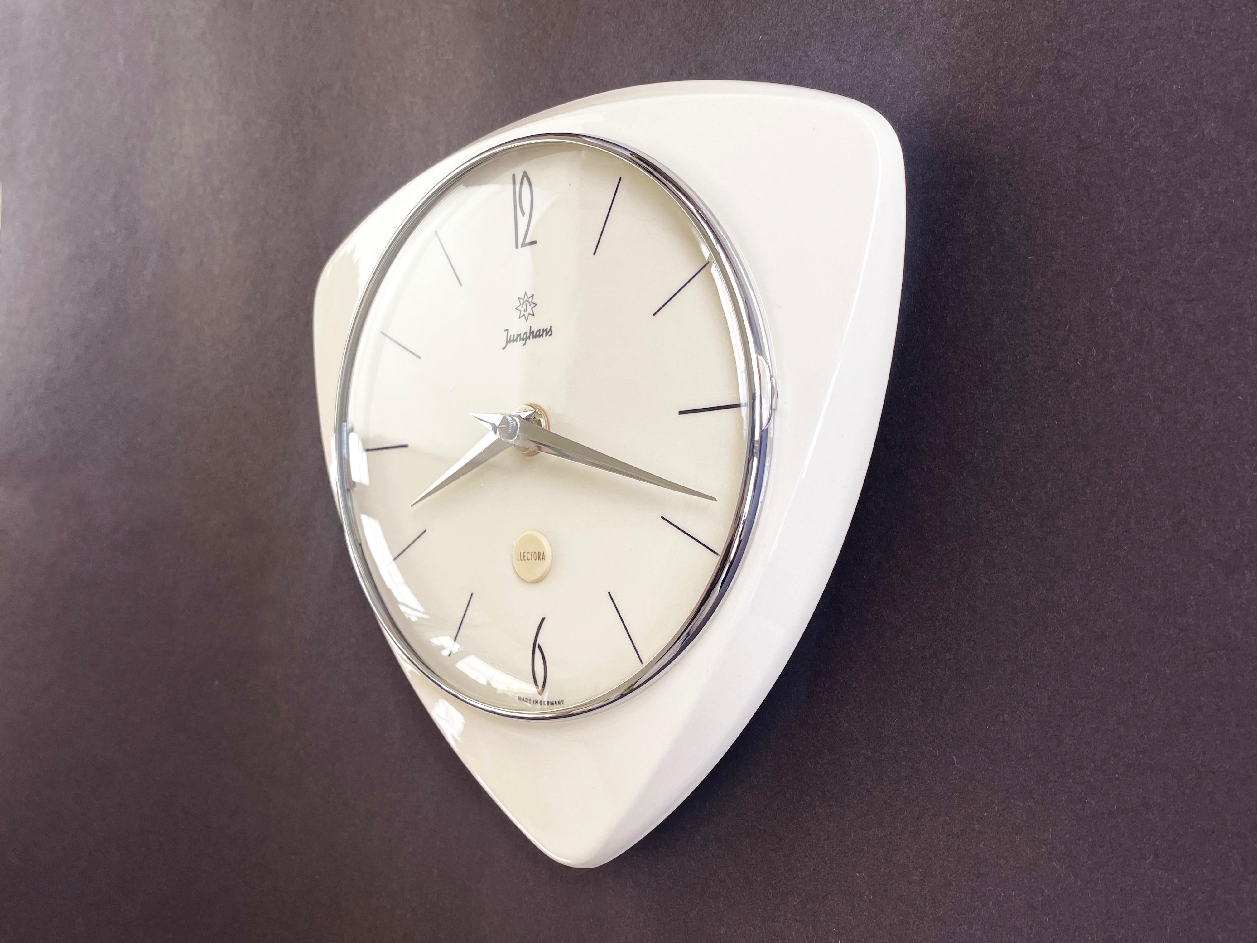 Beautiful triangle wall clock by Junghans, cream ceramic, in a pure 50s original design by 
one of Germanys most renowned clock makers.
Made in the 50s – ''Electora'' by Junghans.
Here with a fish eye glass cover, silver chromed rim, black numbers
