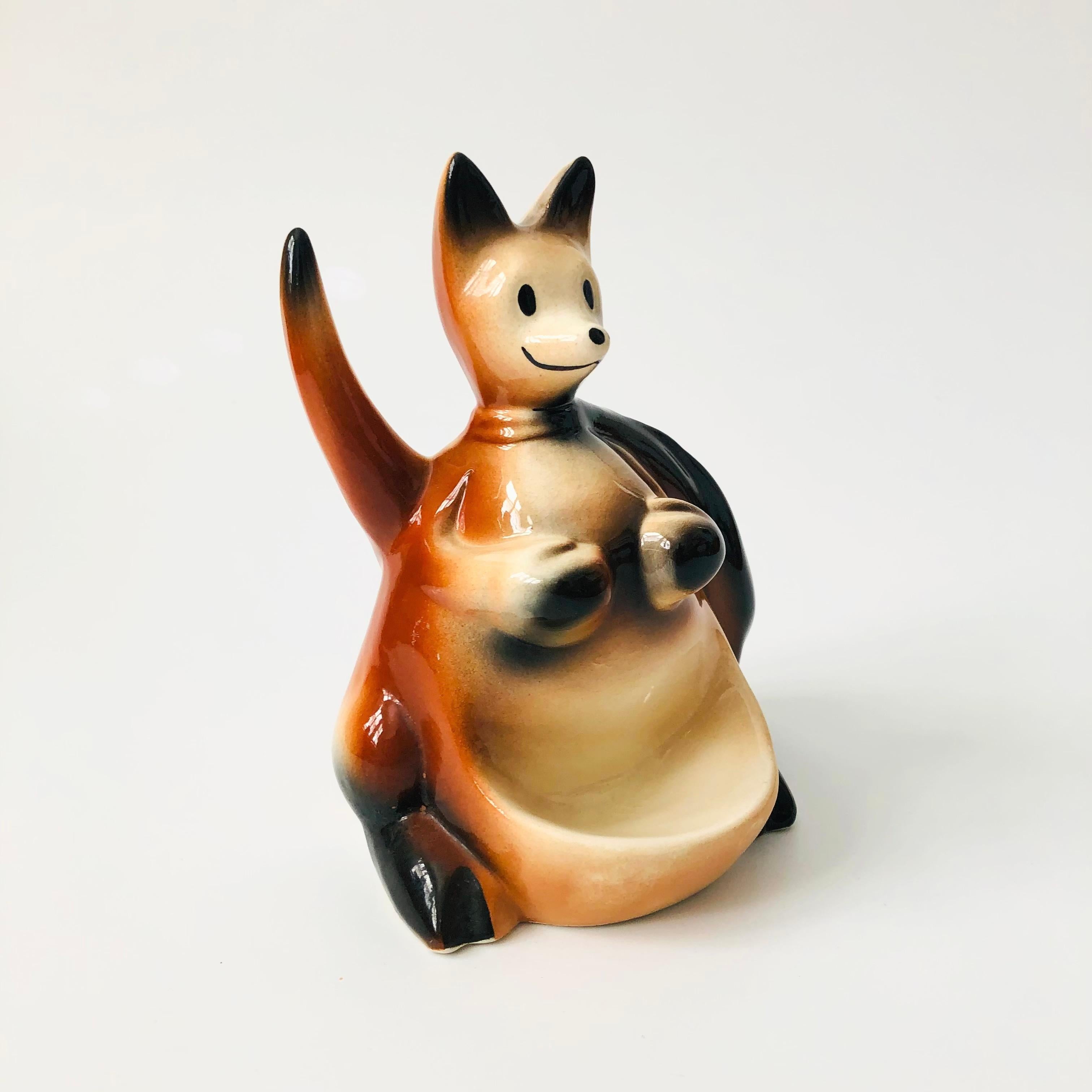 A mid century ceramic organizer/ tray in the shape of a kangaroo. Features a front dish and also a pocket in the back for keeping items. Marked on the back, made in the USA in 1956 by Fine Ent. Inc

