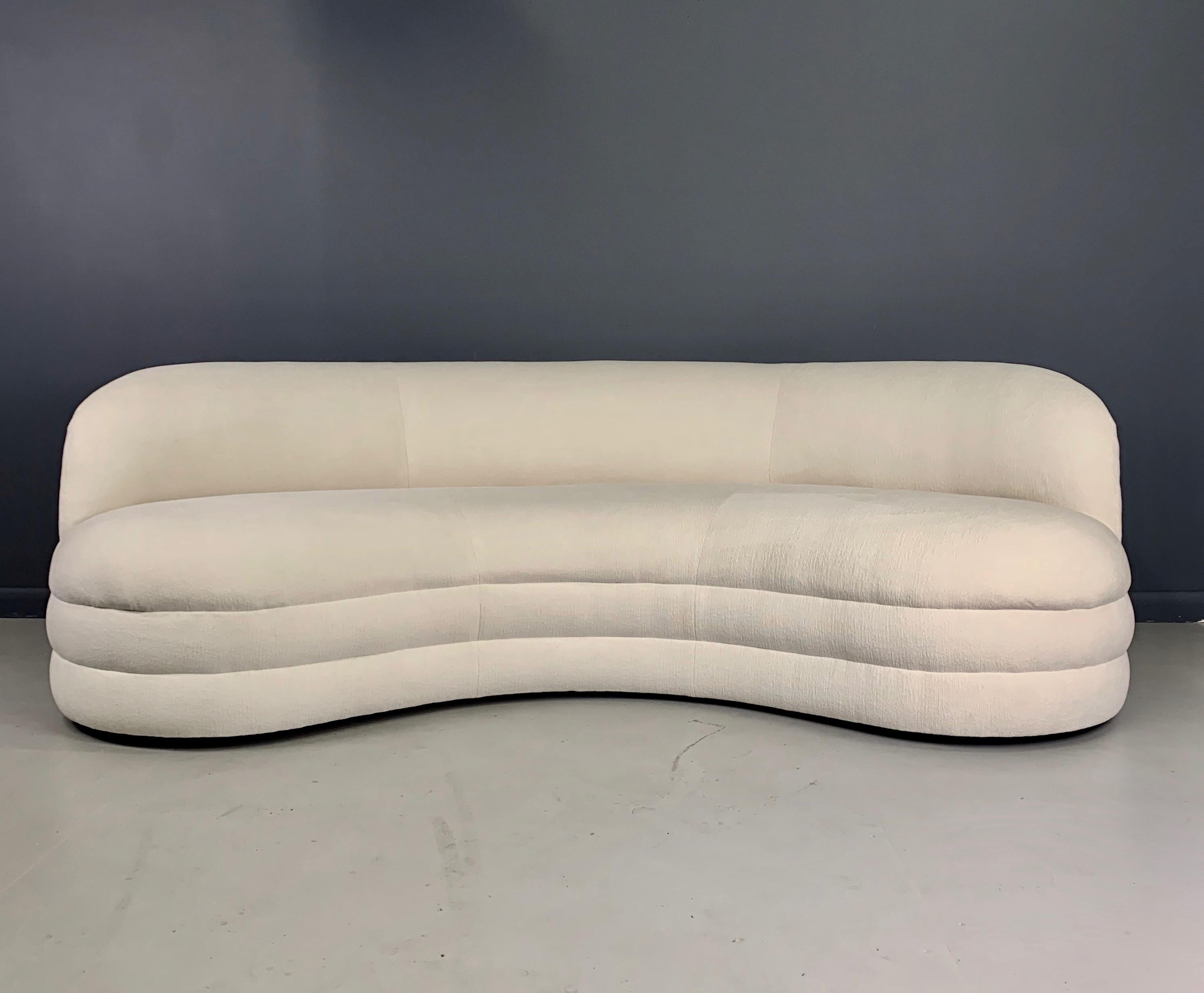 A kidney-shaped sofa that features a nice sculptural modern design, with a curved arched back. These sofas are newly produced and have been handcrafted with a solid hardwood frame, manufactured in the United States with an 7 to 10 week turnaround.
