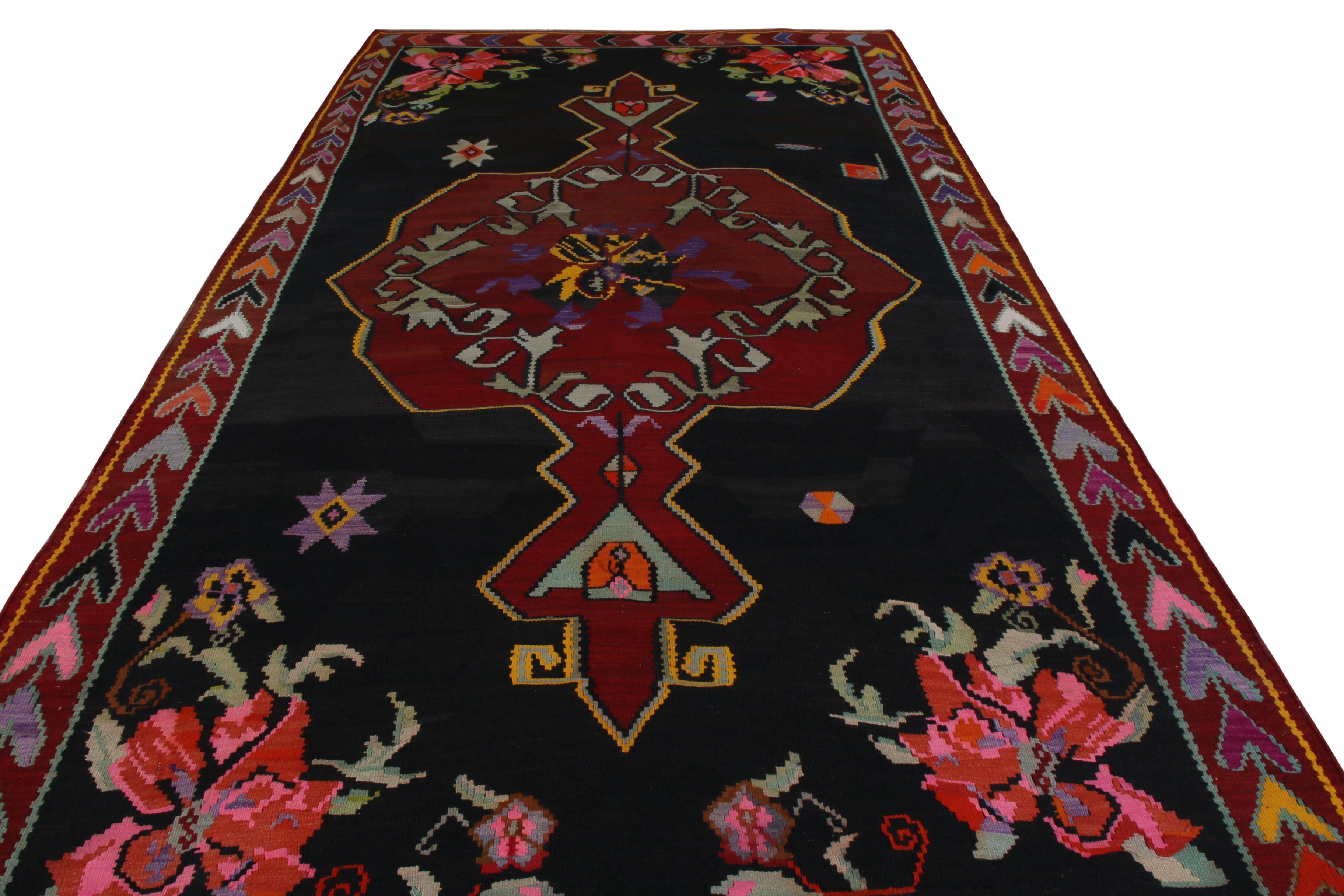 Handmade in wool circa 1950-1960, this vintage flat-weave Kilim rug was created in Turkey. A midcentury Kilim, this design showcases a red medallion pattern surrounding a single flower in pink, purple, and black, with green vines circling the bloom.