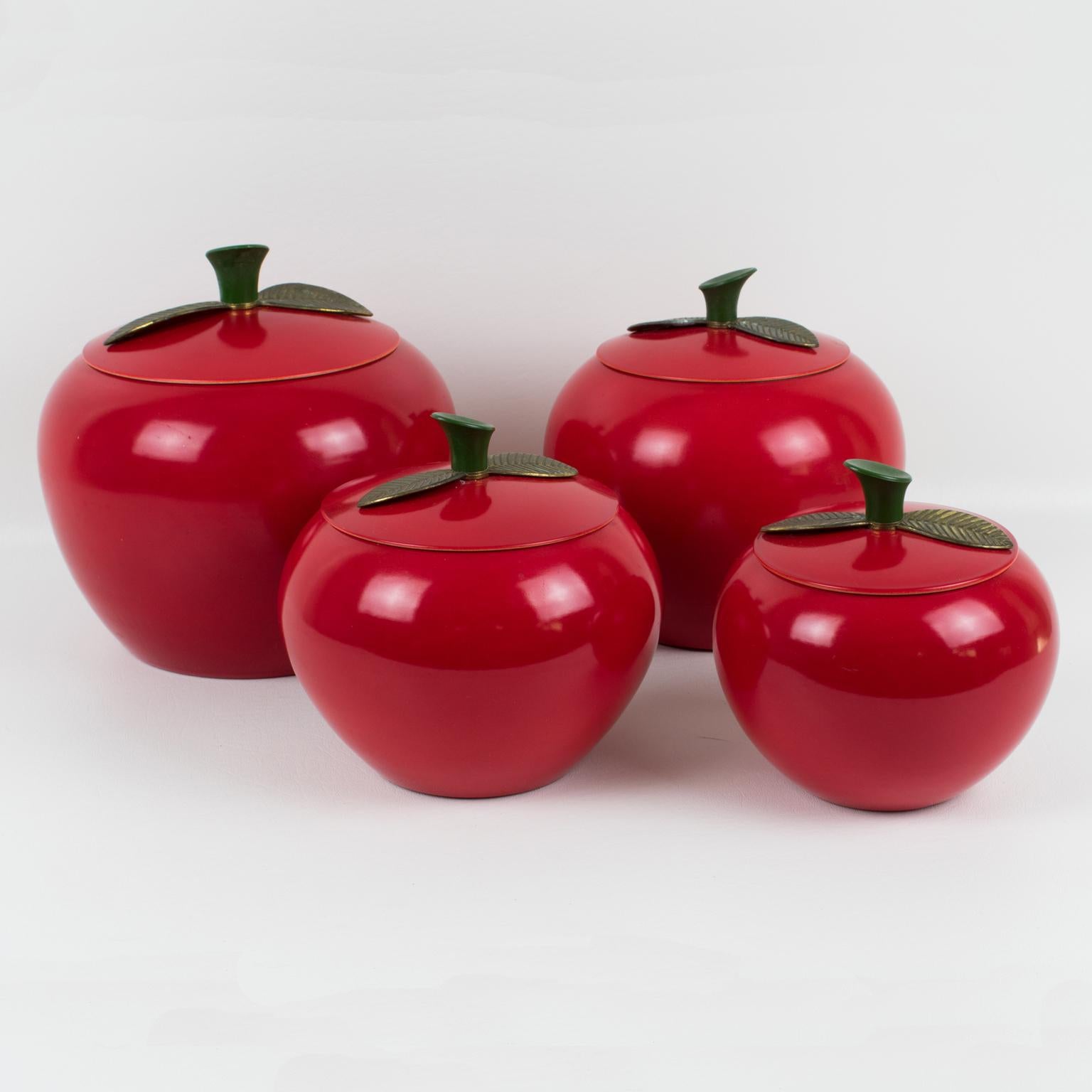 Those cute Mid-Century-Modern 1960s kitchen canister or cookie jar set features an apple-shaped container in red enamel aluminum in assorted graduated sizes. You have four pieces in this set. The containers are adorned with a stem in hard green