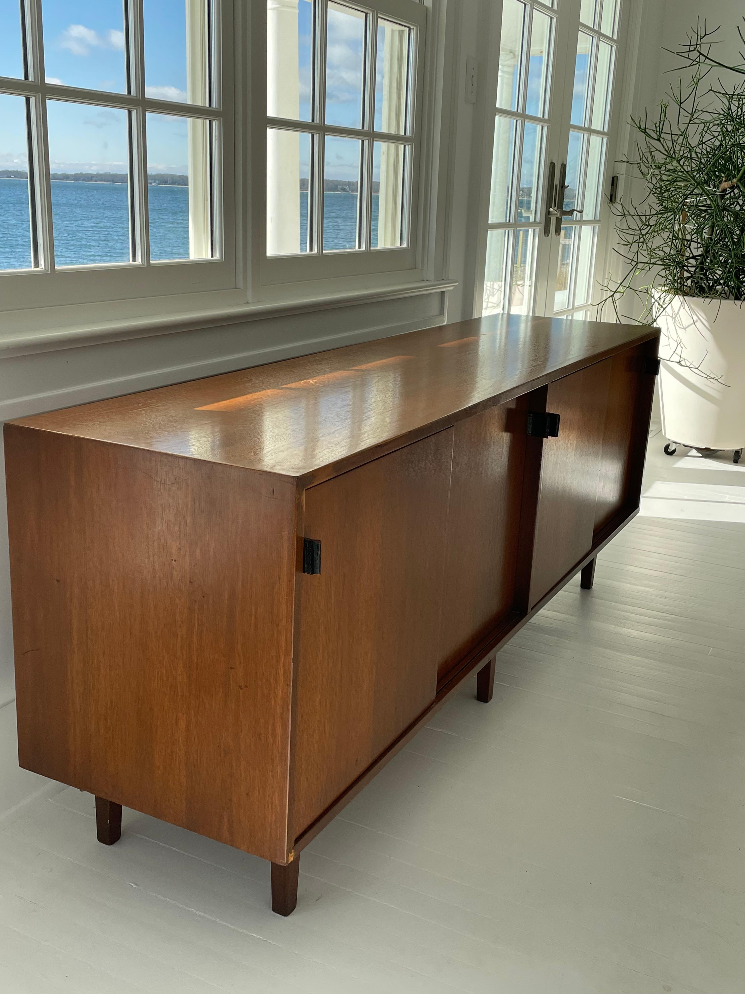 This elegant and classic Mid Century understated Knoll credenza has four sliding doors with original leather pulls and adjustable wood shelves. This seems to be an early piece with rare wood square legs . A real beauty! Very good condition.