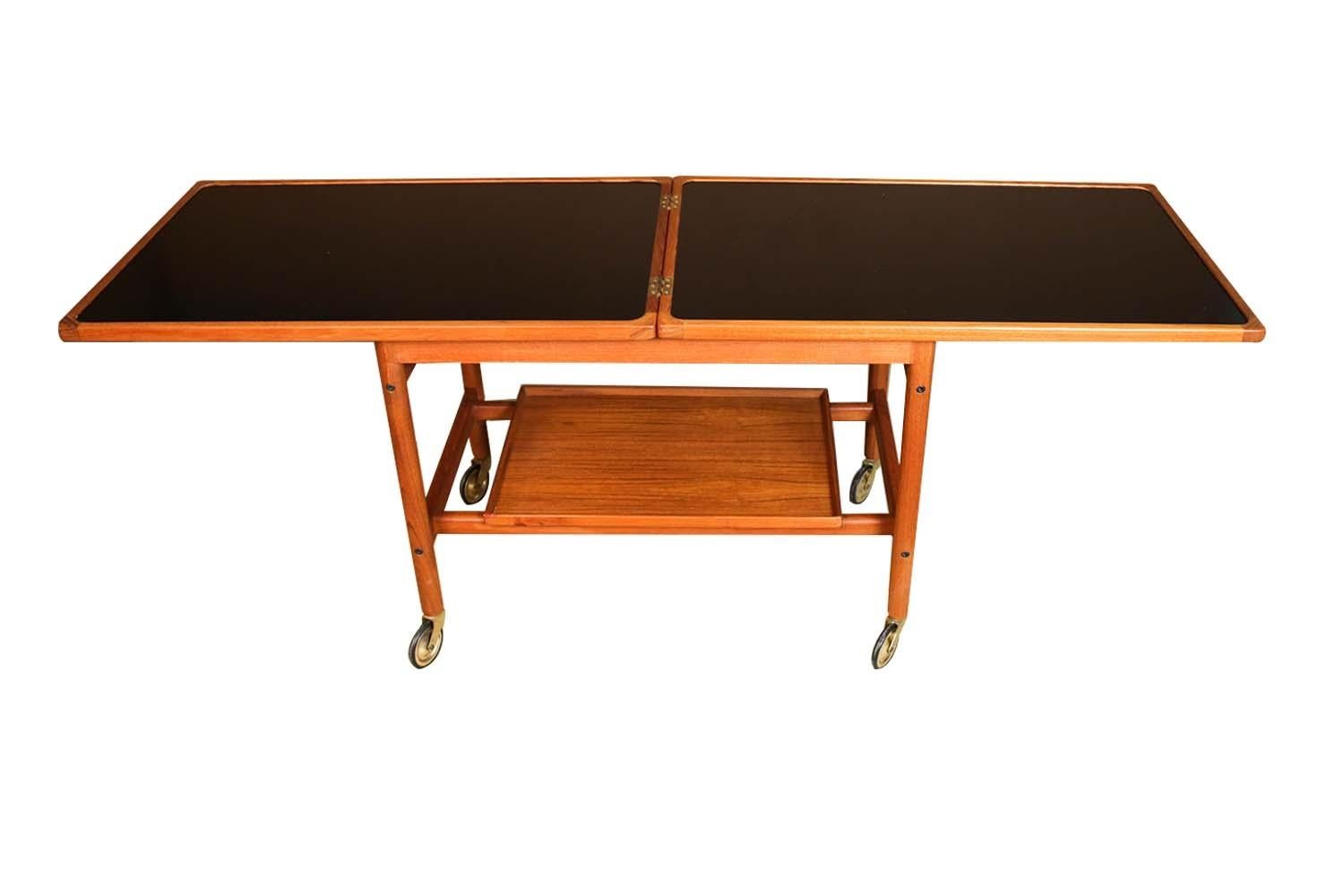 An exceptional Mid-Century Modern serving bar cart by designer Kurt Ostervig for Jason Mobler in Denmark, circa 1960s. Beautifully crafted from teak, this cleverly designed piece features a sliding upper shelf and removable lower tray. The beautiful