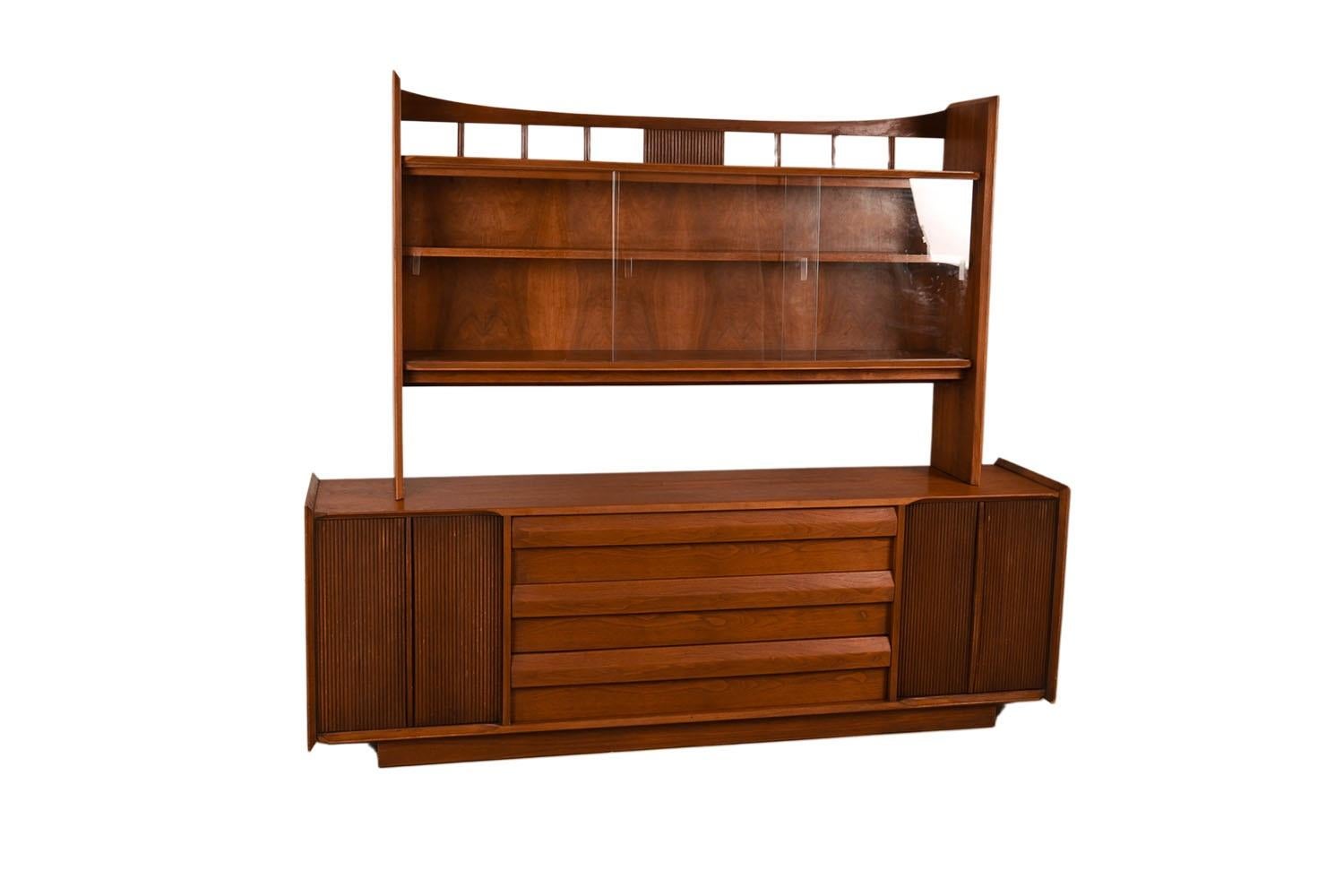 An elegant long Lane First Edition Mid-Century Modern sculpted walnut credenza/sideboard with detachable glass hutch. This is a beautiful example of Mid-Century craftsmanship by Lane Furniture Scandia line, First Edition Buffet Credenza, with