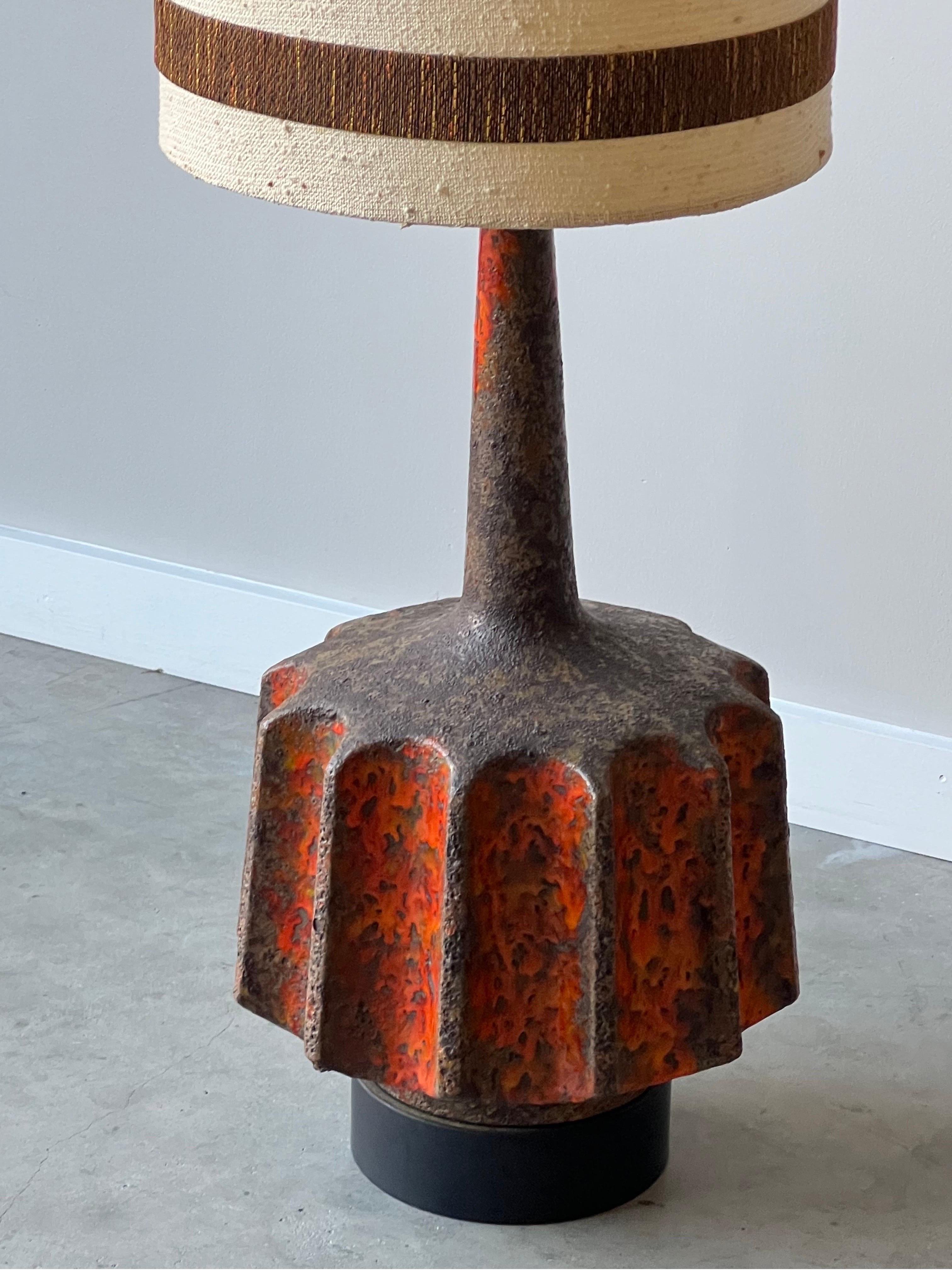 Mid-century massive brutalist ceramic lava glaze lamp, made circa 1960s. This table lamp is an absolute statement piece. Bright orange coloration, heavily textured due to the lava glaze, and large stature. Equipped with the original shade, also