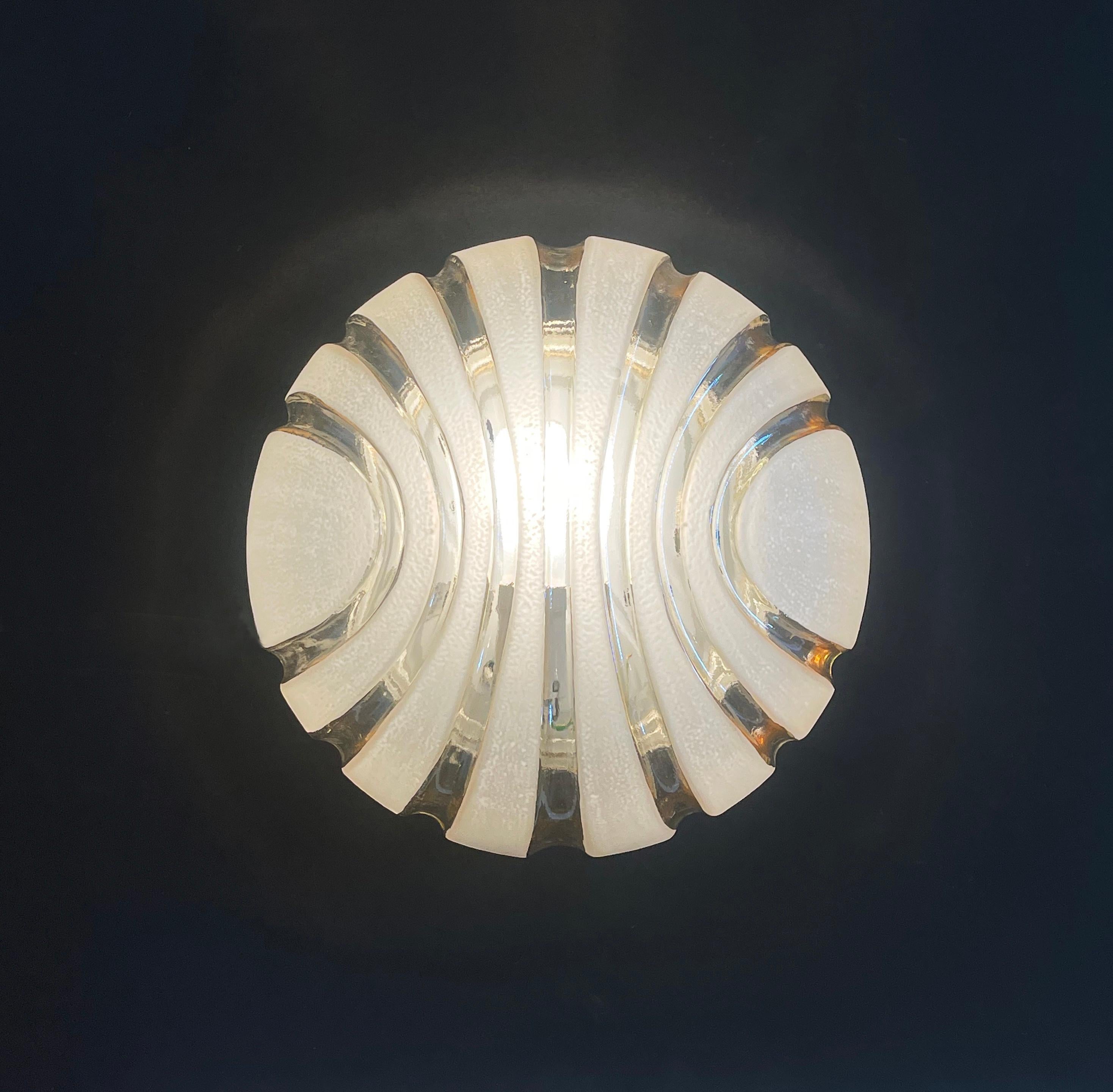 Wunderschön gestaltete Wand- oder Deckenleuchte, die in den späten 70er Jahren von Massive Lighting in Belgien hergestellt wurde.
Psychedelische bernsteinfarbene Lavaströme fließen an den Seiten hinunter, vorbei an erhöhten sandgestrahlten